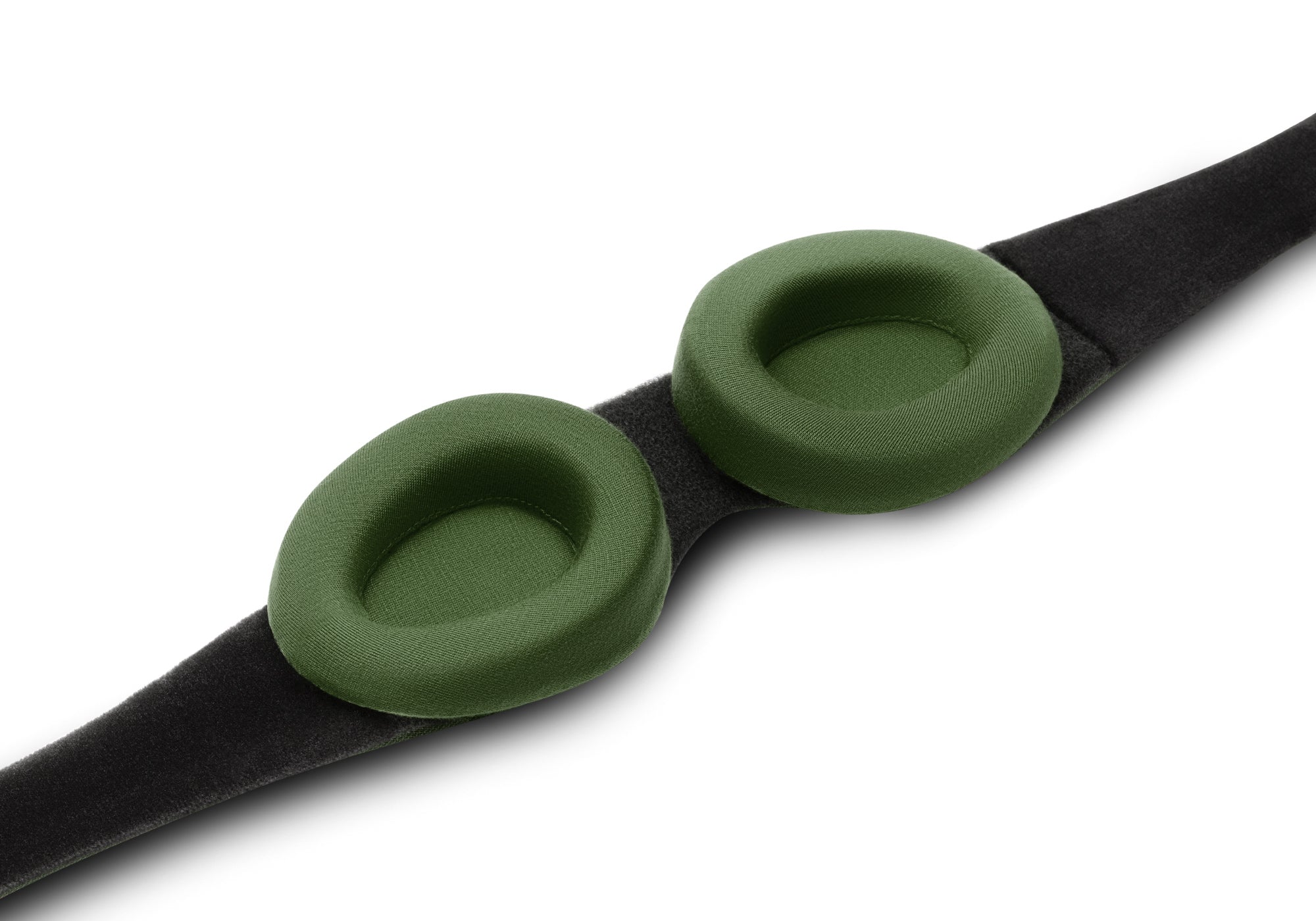 A close-up, high-angle view of the interior side of a black Manta Sleep Mask strap laid diagonally on a white surface, showcasing two thick, cushioned, and contoured forest green fabric eyecups.