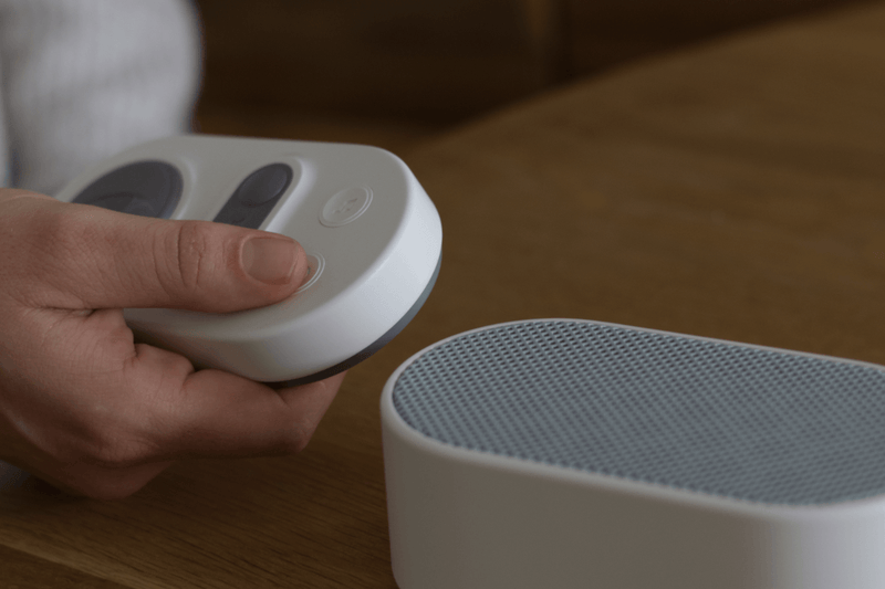 A close-up shot of Stone White Manta White Noise Machine standing on a table, with a hand pressing a button on a remote pad.