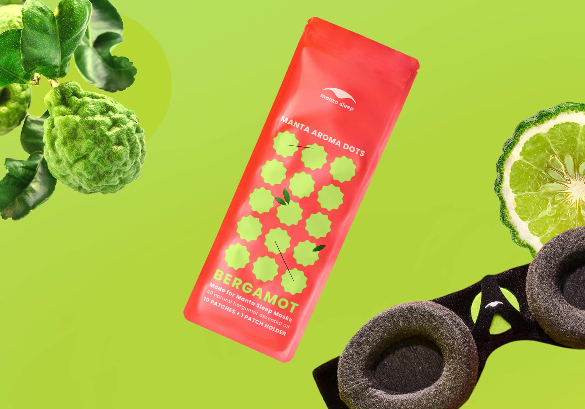 Bergamot-scented Manta Aroma Dots packaging floating with whole and sliced bergamot fruit next to a sleep mask, on a lime green background.