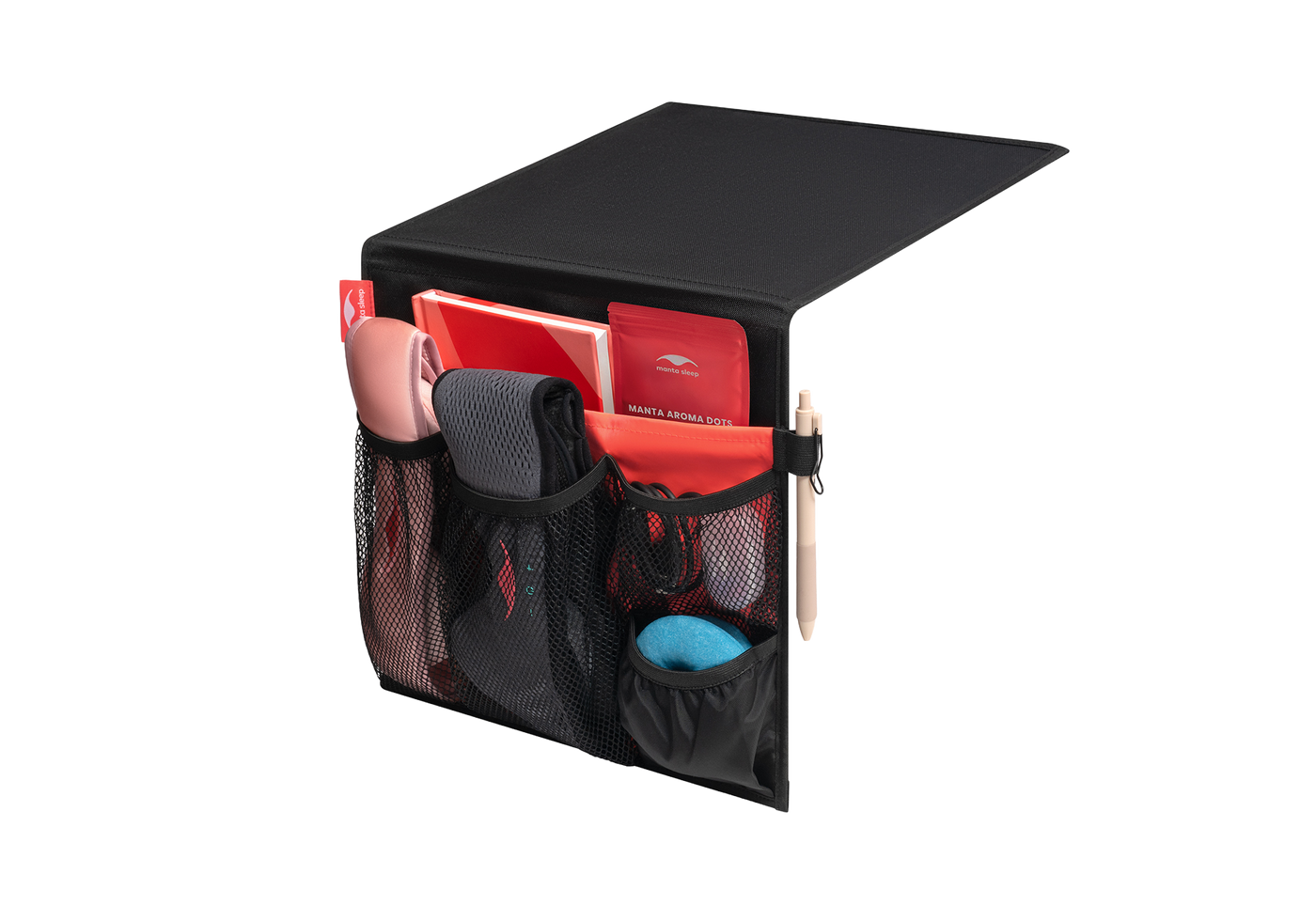 Studio shot of a black and coral Manta Bedside Caddy filled with sleep masks, a notebook, and a pen, isolated on a white background.