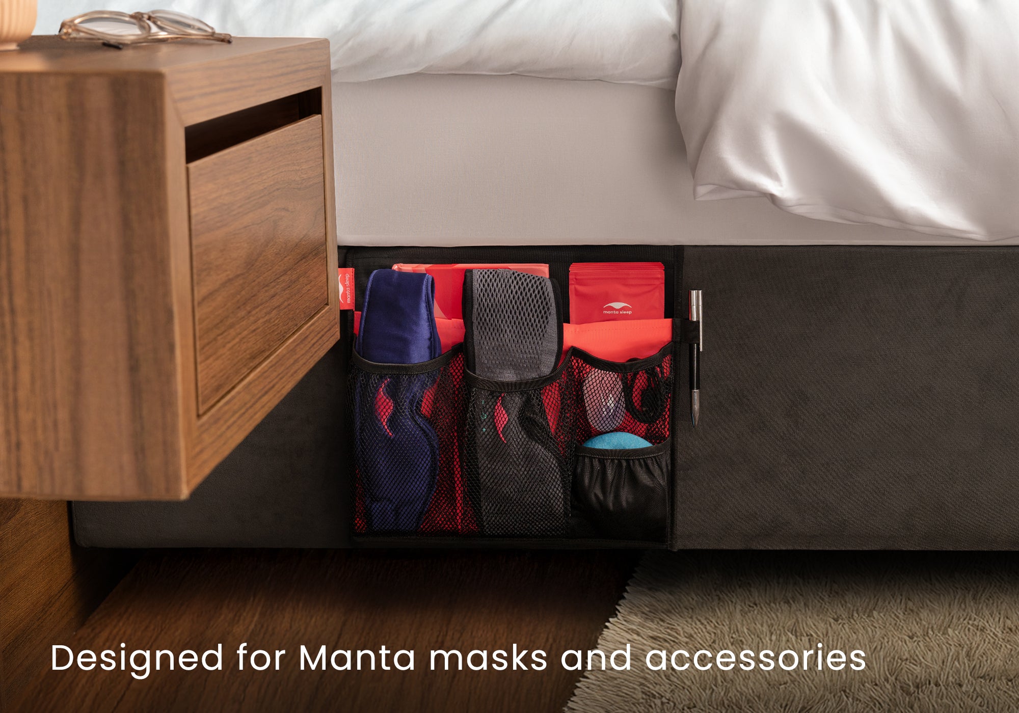 Front view of a black Manta Bedside Caddy holding sleep masks, a journal, and a pen. Text overlay reads "Designed for Manta masks and accessories".