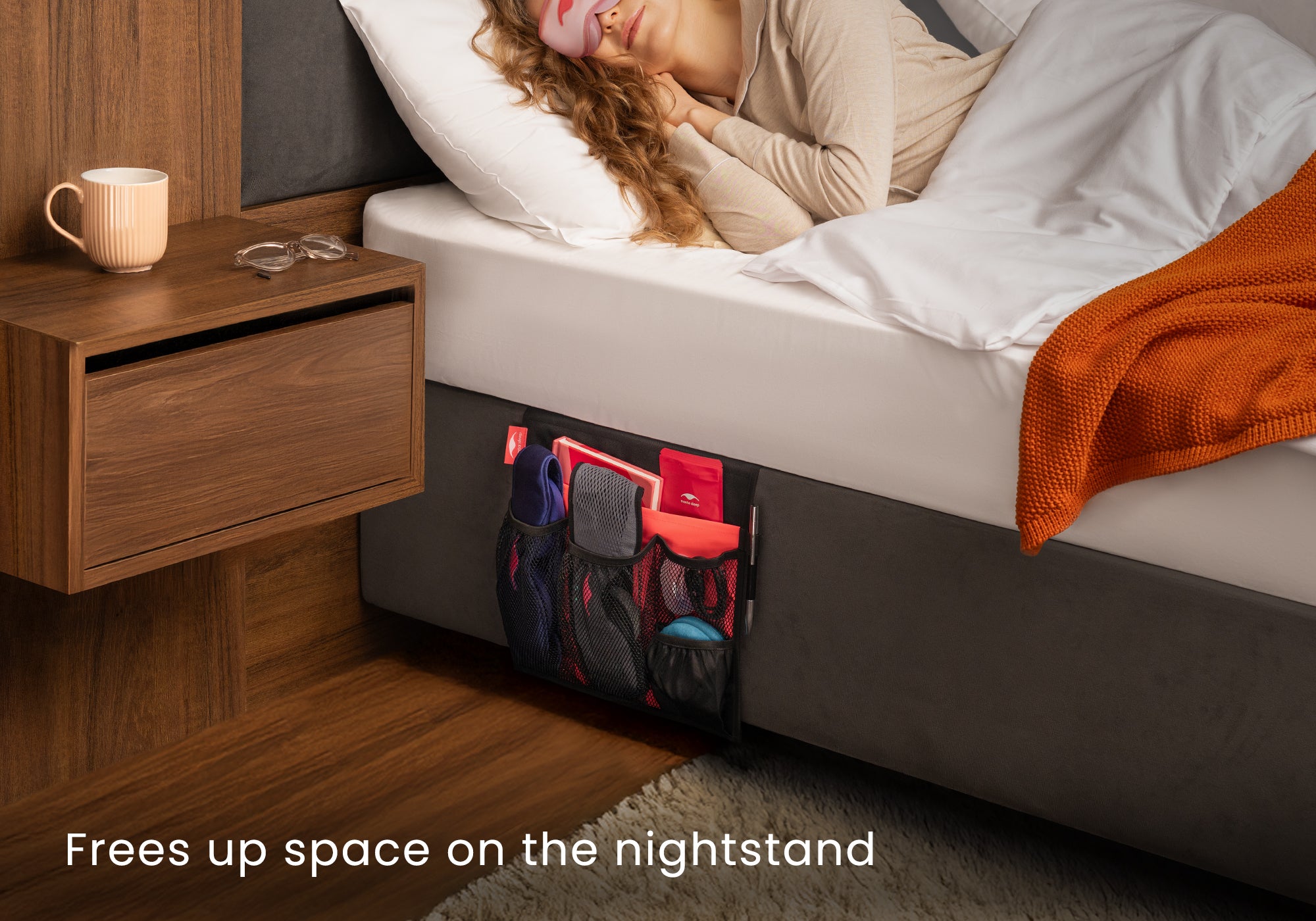 A woman sleeping in a bed equipped with a black Manta Bedside Caddy full of items. Text overlay reads "Frees up space on the nightstand".