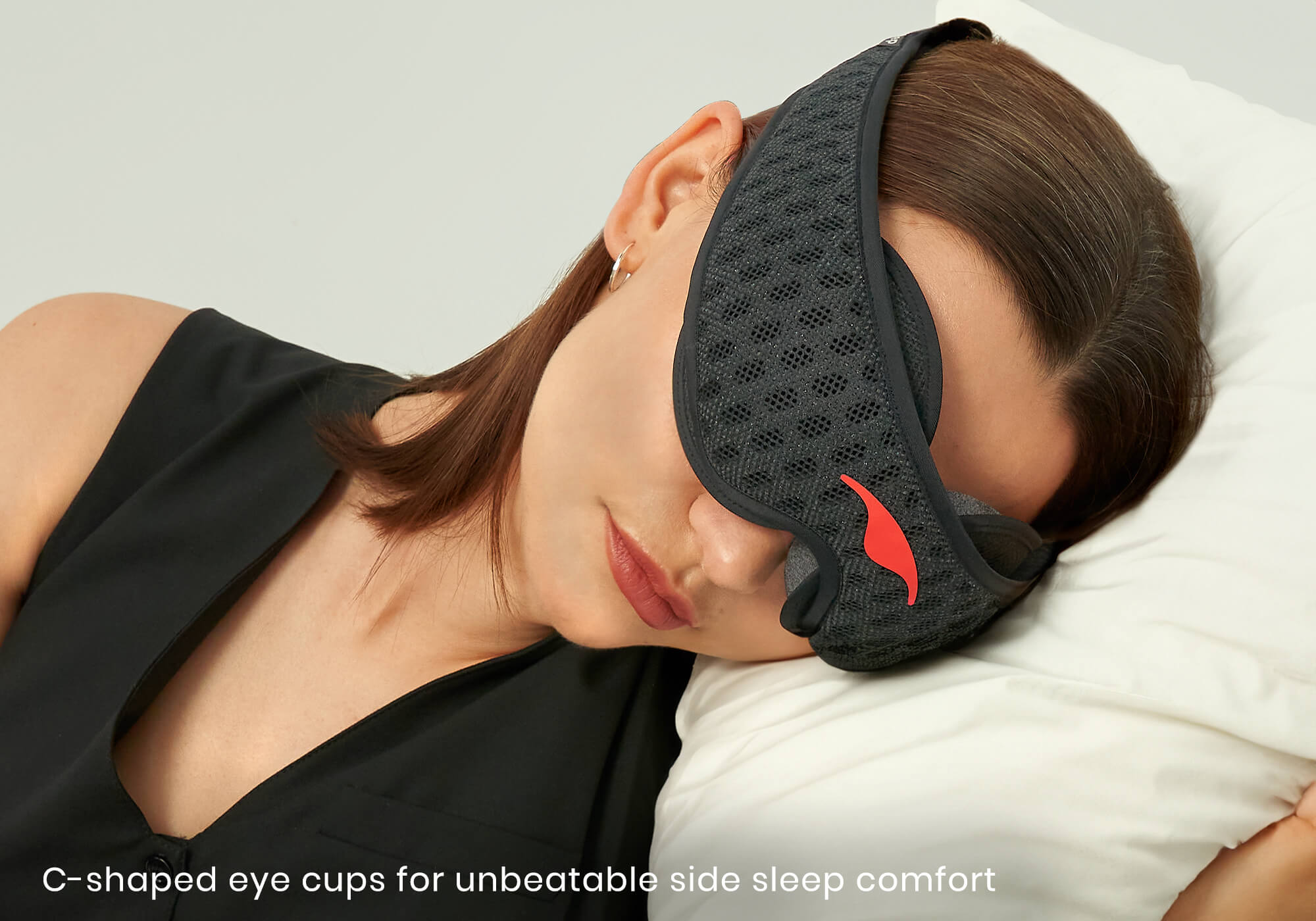 Close-up of a person sleeping on a white pillow wearing a Carbon Black Manta Sleep Mask PRO, with caption "C-shaped eye cups for unbeatable side sleep comfort".