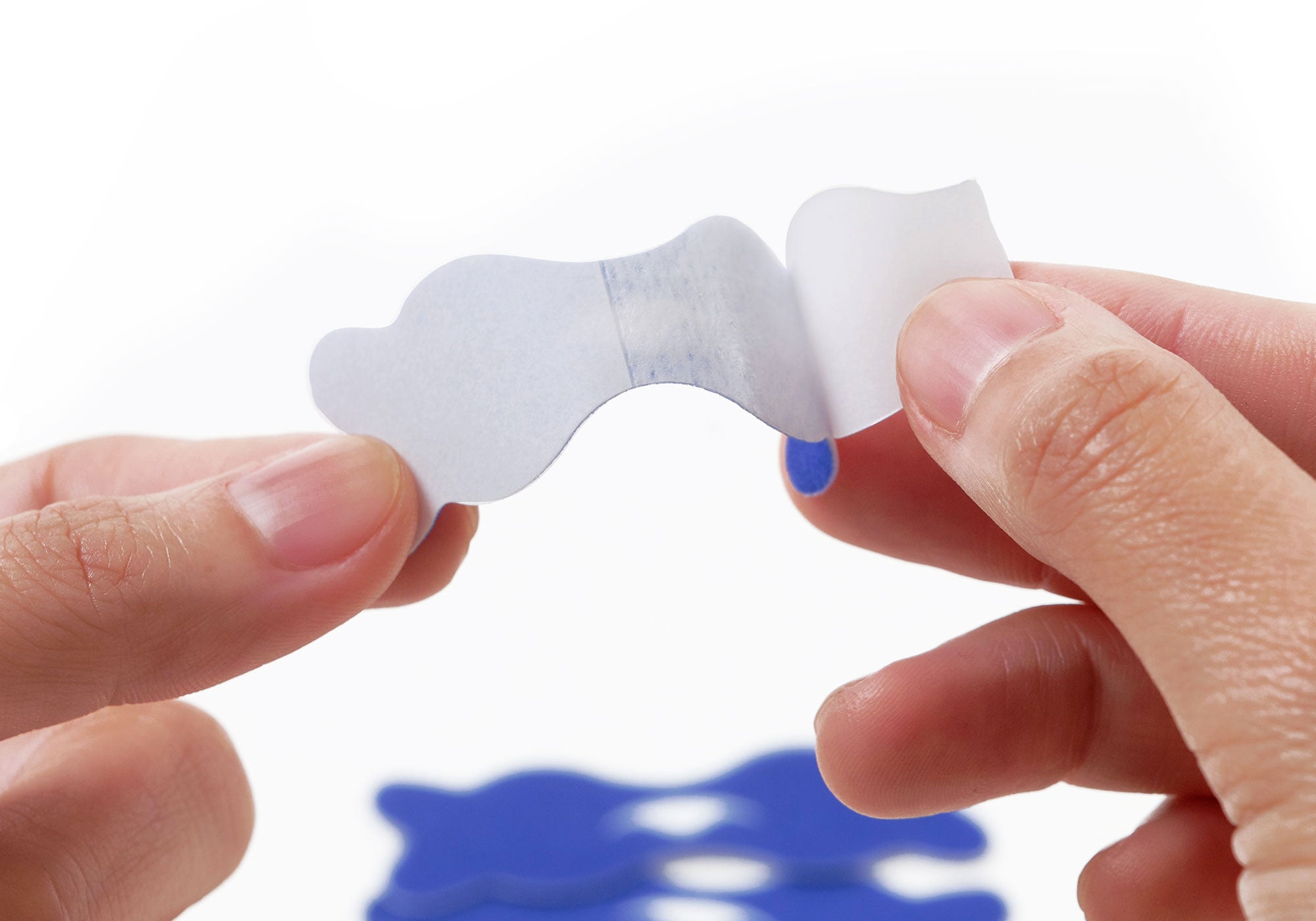Close-up shot of hands peeling a white protective backing paper off a blue Manta nasal strip.