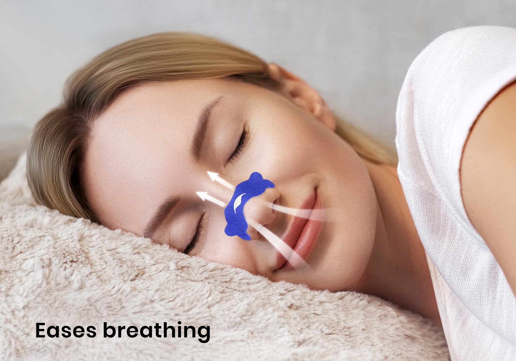 Close-up of a smiling woman sleeping on a plush pillow with a blue nasal strip on her nose and airflow graphics. Text overlay: "Eases breathing".