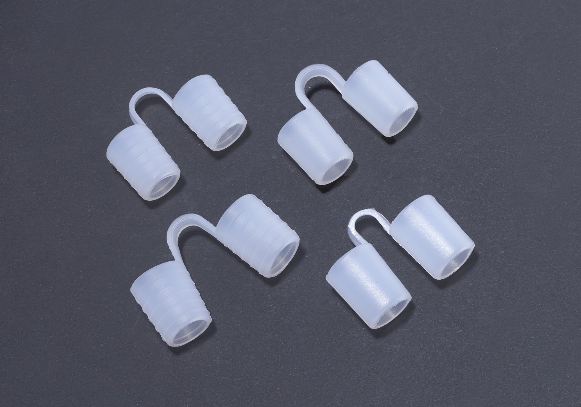 Overhead view of a set of four translucent silicone anti-snore nose vents arranged on a dark grey background.