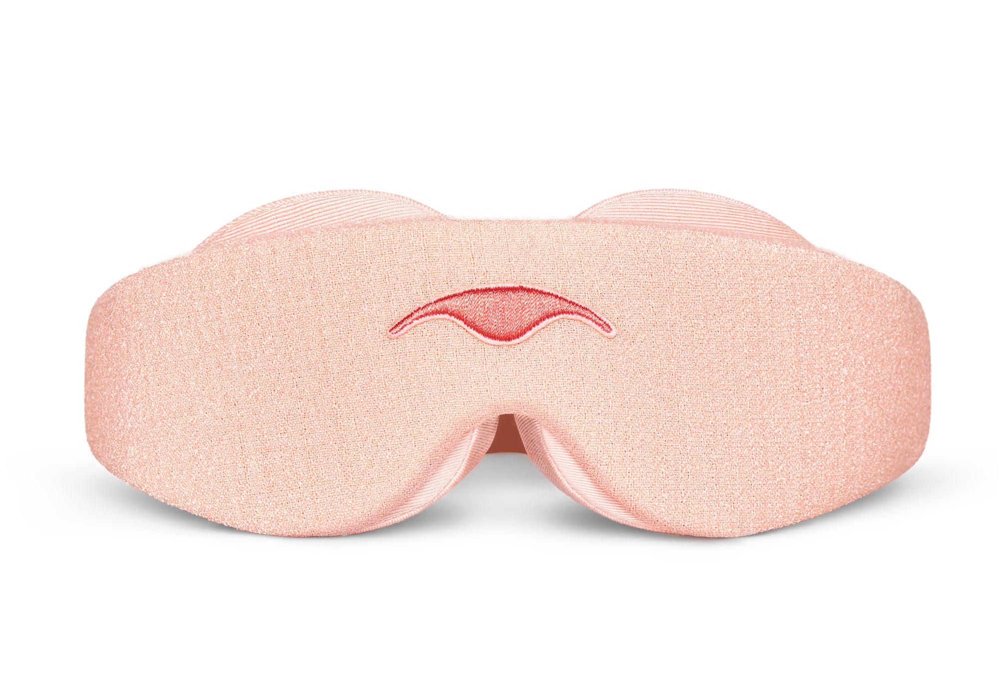 Direct front view of the Sunrise Pink Manta Sleep Mask laid flat against a white backdrop, showing its contoured shape, light pink fabric texture, and a centered, embroidered pink Manta Sleep logo.