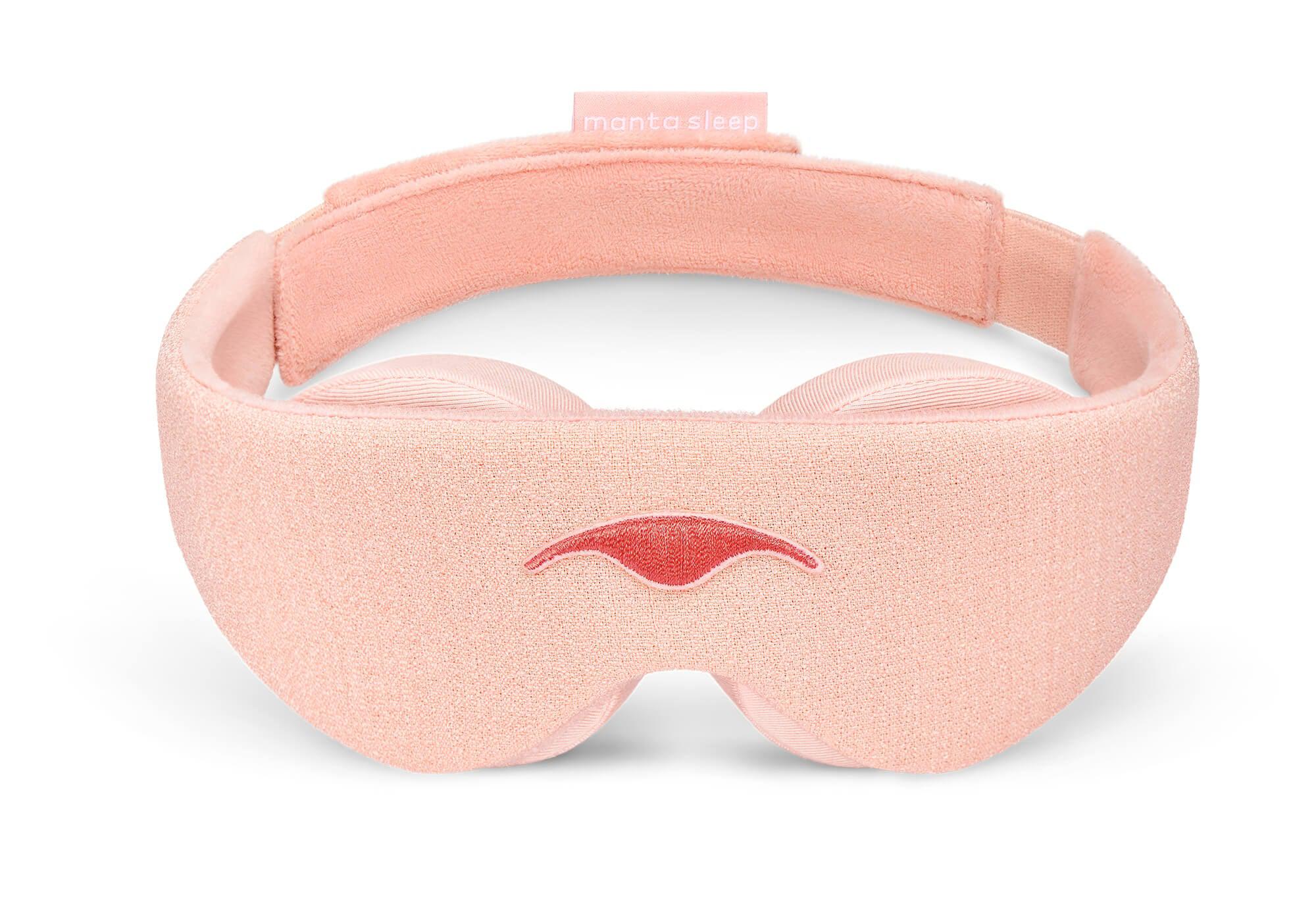 Front view of the Sunrise Pink Manta Sleep Mask arranged in a freestanding circle against a plain white background. The textured light pink mask features a darker pink embroidered Manta Sleep logo in the center and a small pink brand label attached to the back strap.
