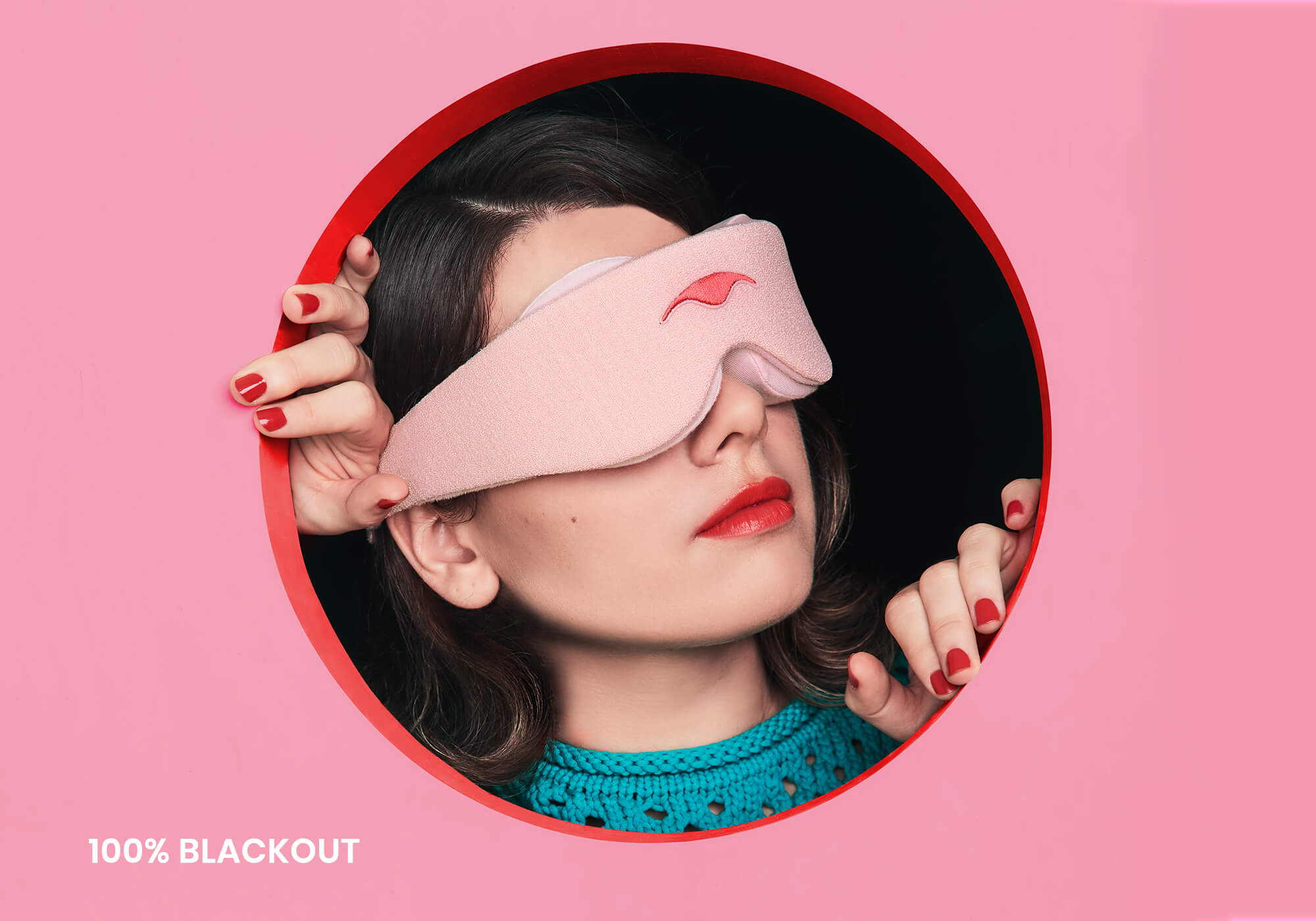 A person wearing a light pink Manta Sleep Mask looks slightly upward while framed inside a circular cutout against a pink wall. Their hands with red nail polish grip the edges of the circle against a dark backdrop, and the white text "100% blackout" is displayed in the lower left corner.
