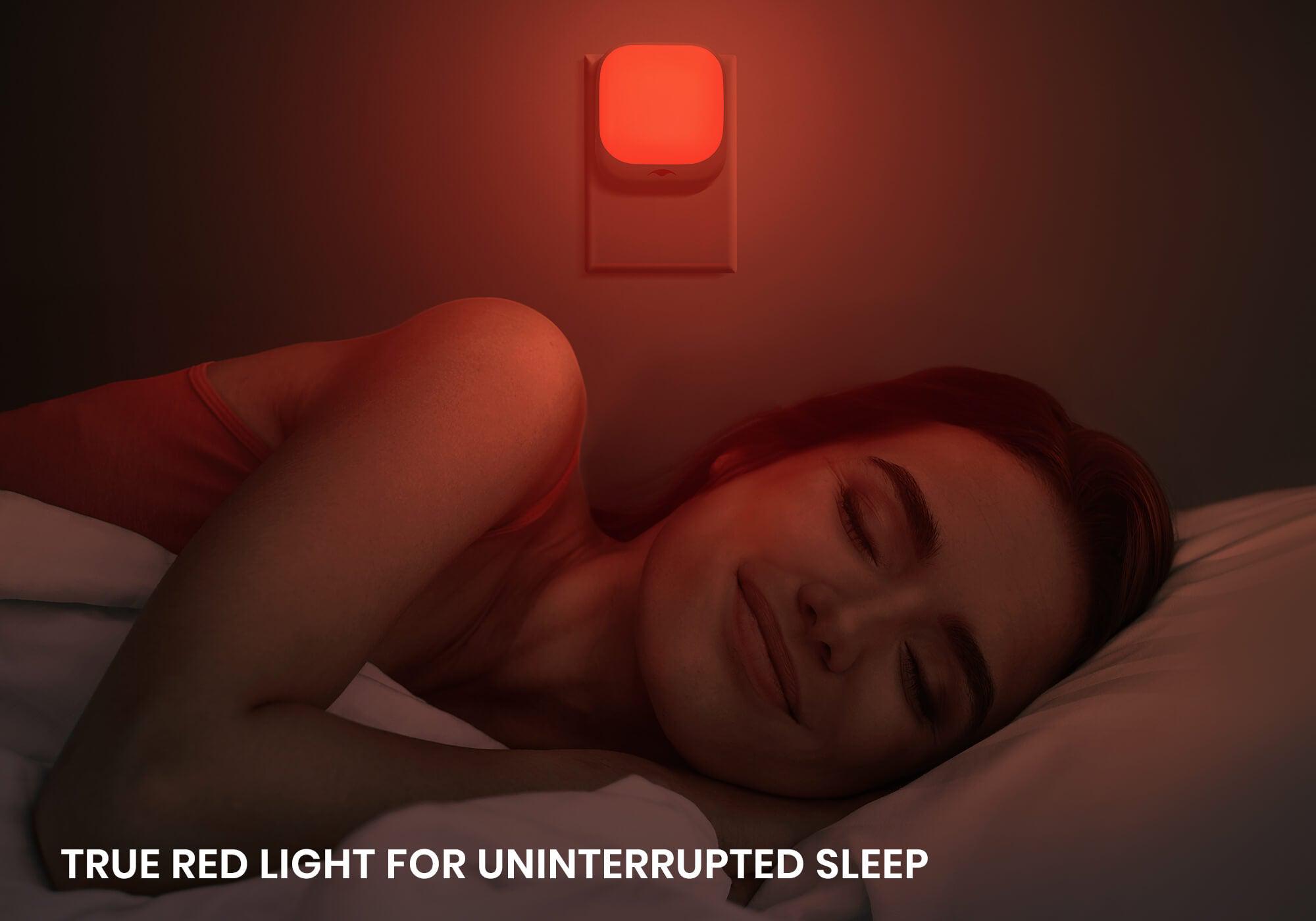 A woman sleeping peacefully in a dark bedroom illuminated by the soft red glow of a wall-mounted Manta Sleep night light.