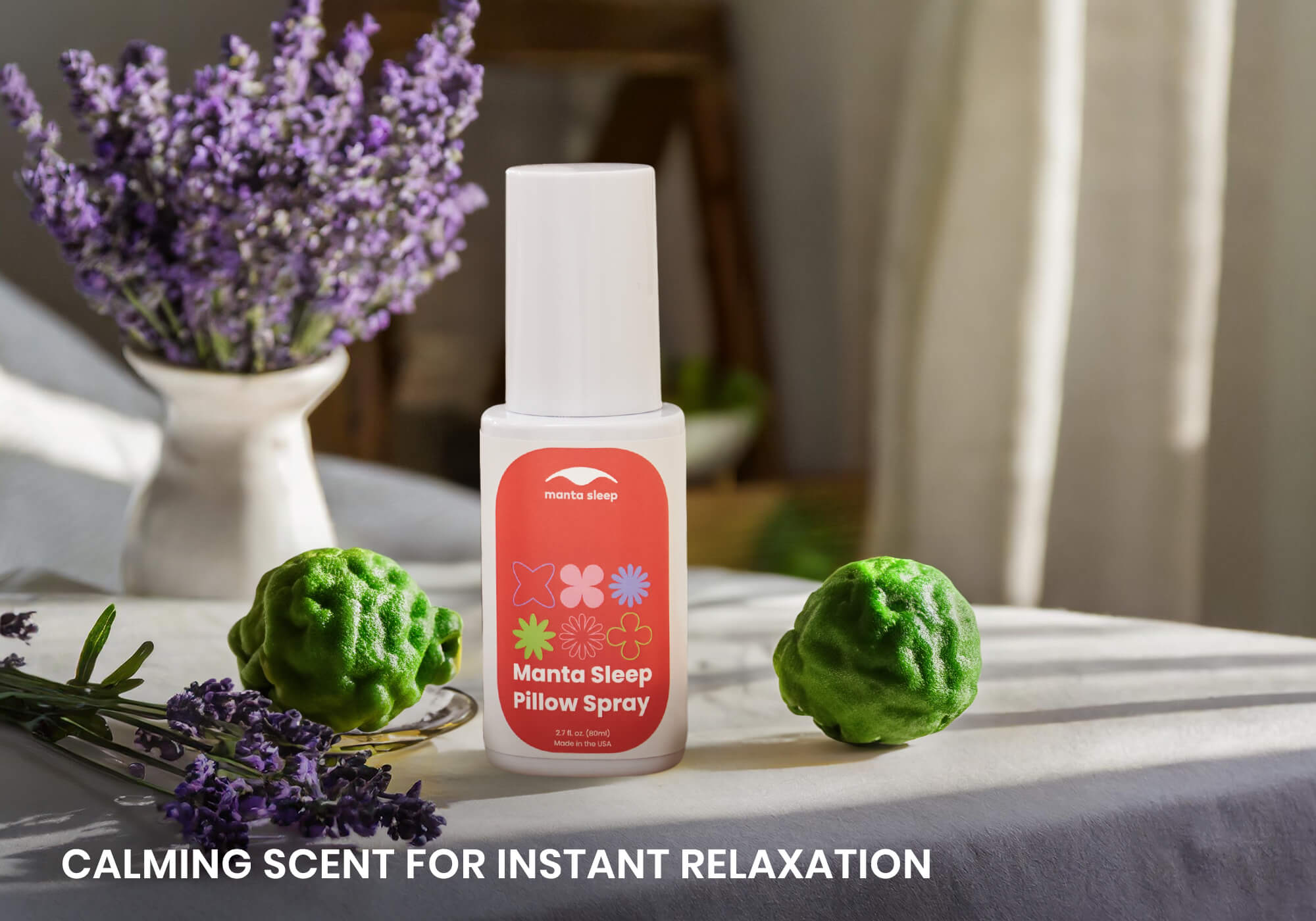 Manta Sleep Pillow Spray bottle on a sunlit table next to lavender flowers and green bergamot citrus fruit. Text: Calming scent for instant relaxation.