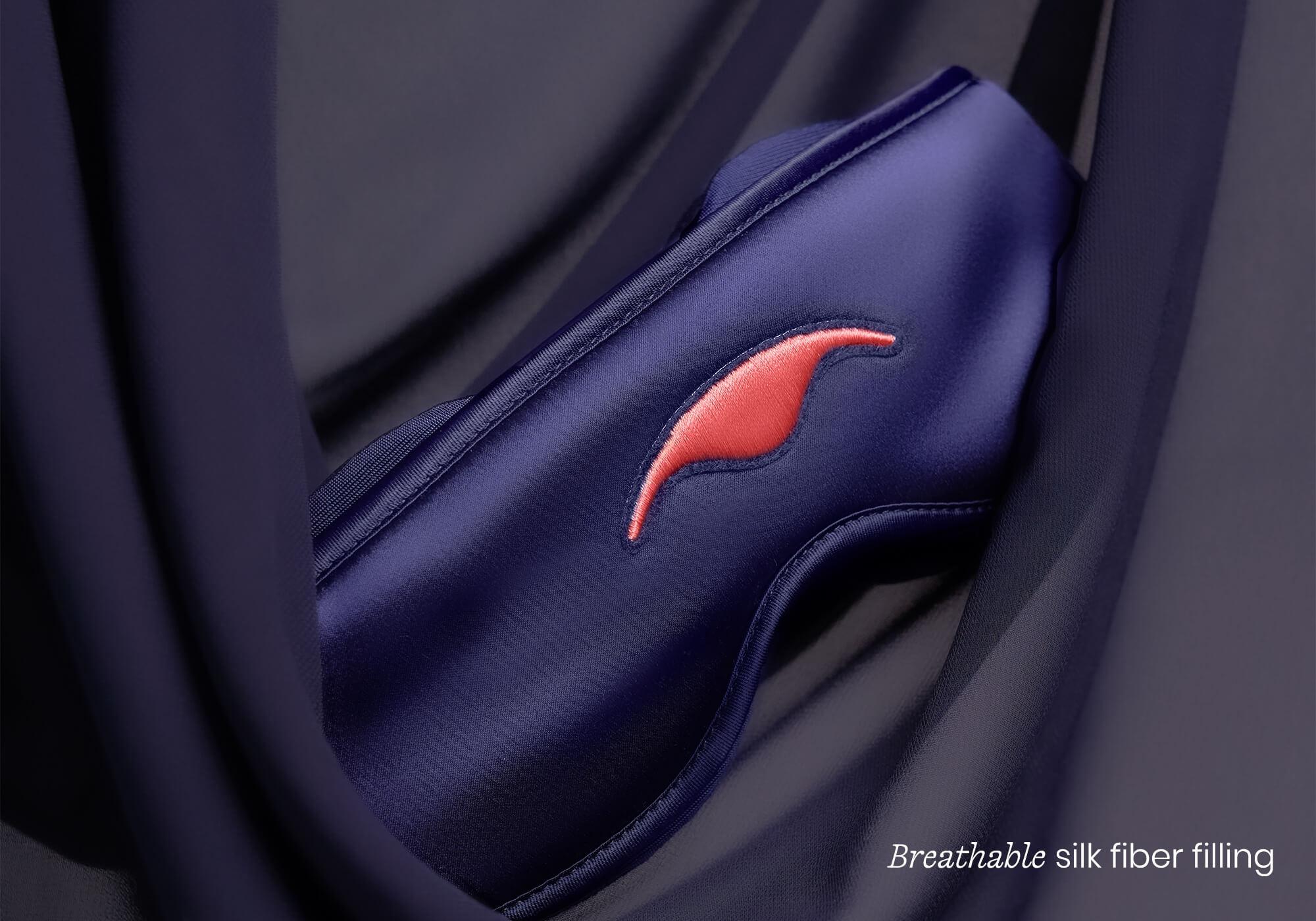 Macro shot of the padded, purple silk sleep mask nestled in soft folds of matching fabric, captioned "Breathable silk fiber filling".