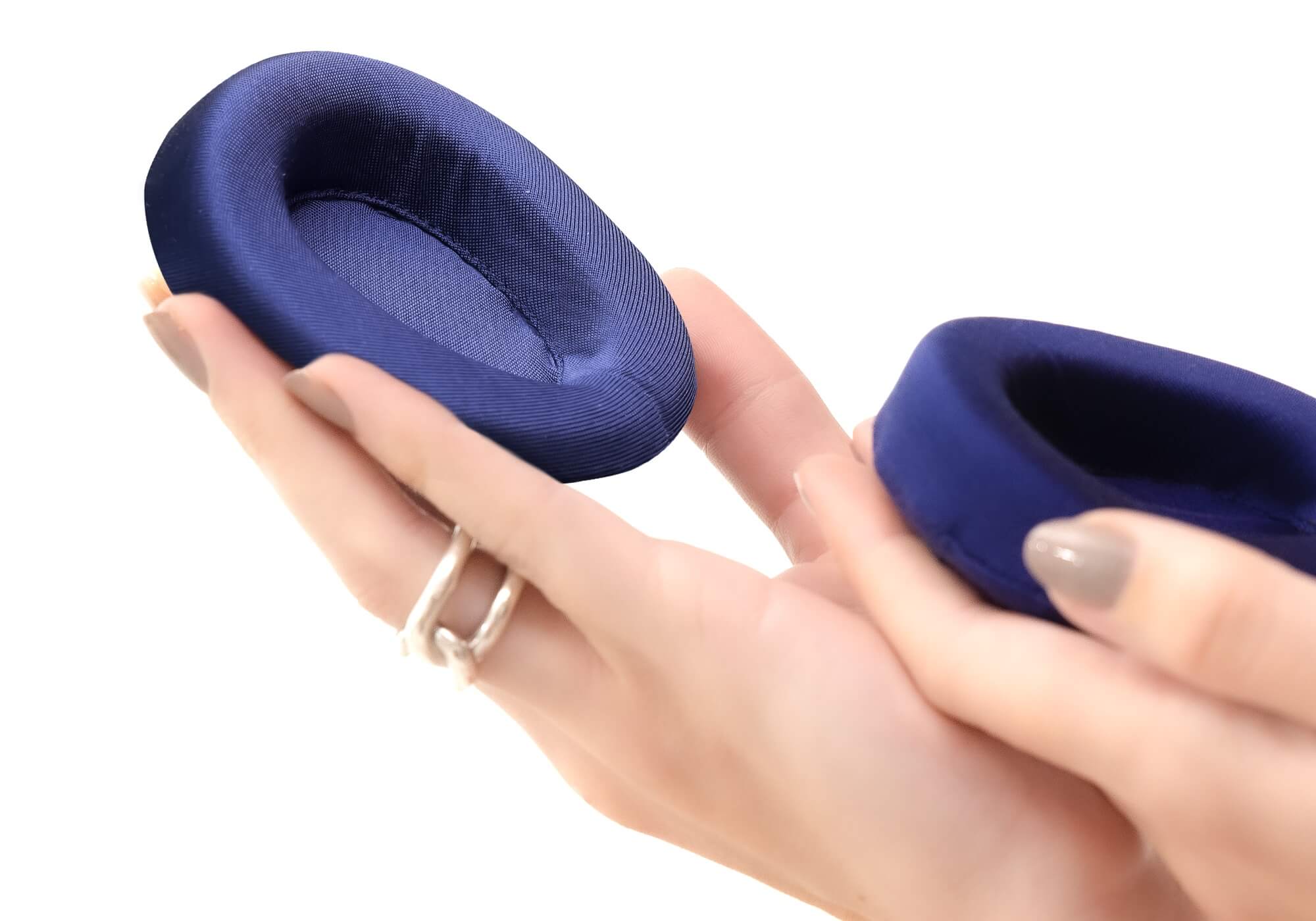Close-up of a person's hands holding two detachable, padded purple silk eye cups against a bright white background.