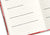 Close-up shot of the white pages inside a red journal, displaying printed reflection questions above blank writing lines.