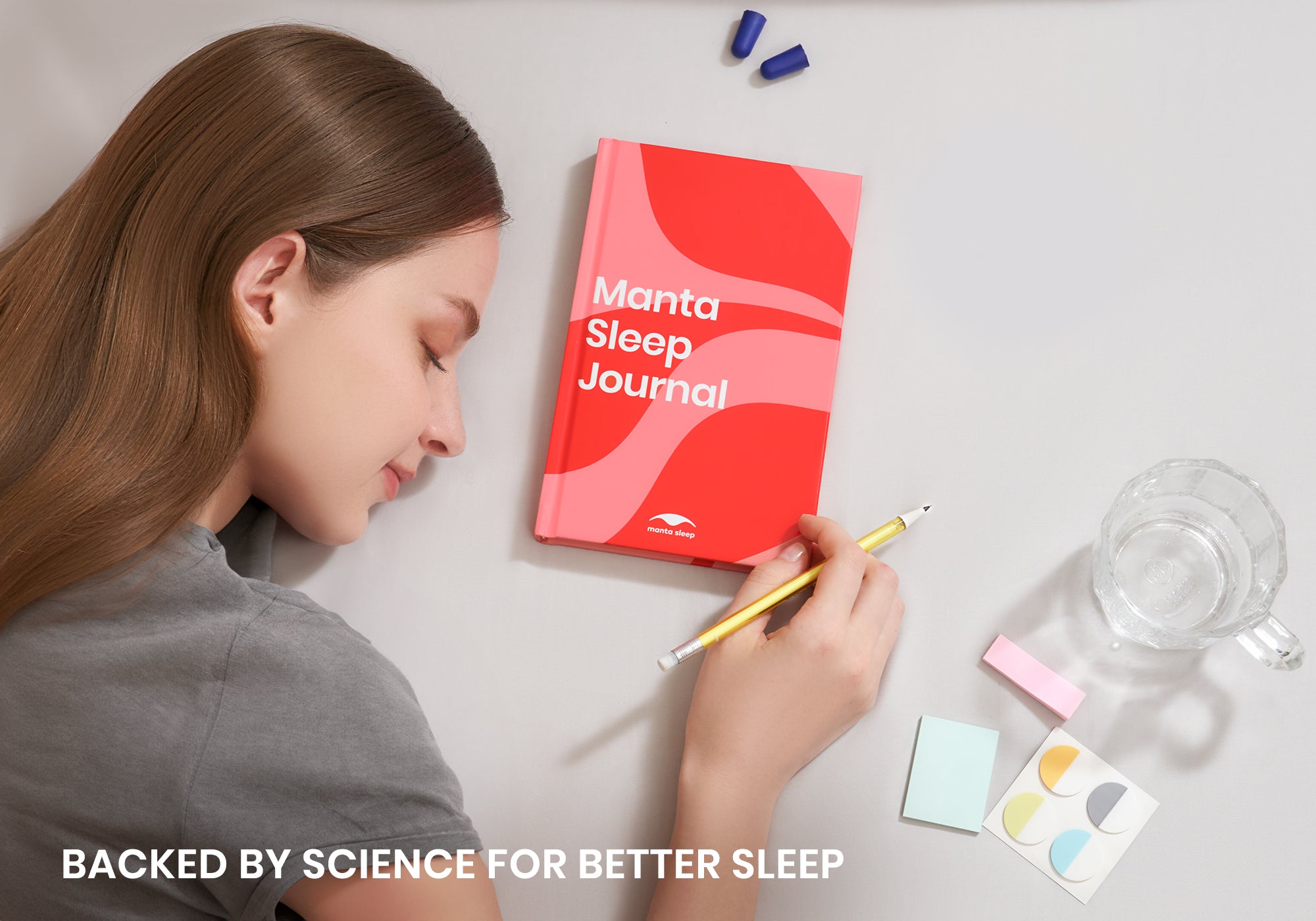 Overhead shot of a woman with closed eyes resting near a red Manta Sleep Journal, holding a pencil. Text overlay reads "Backed by science for better sleep".