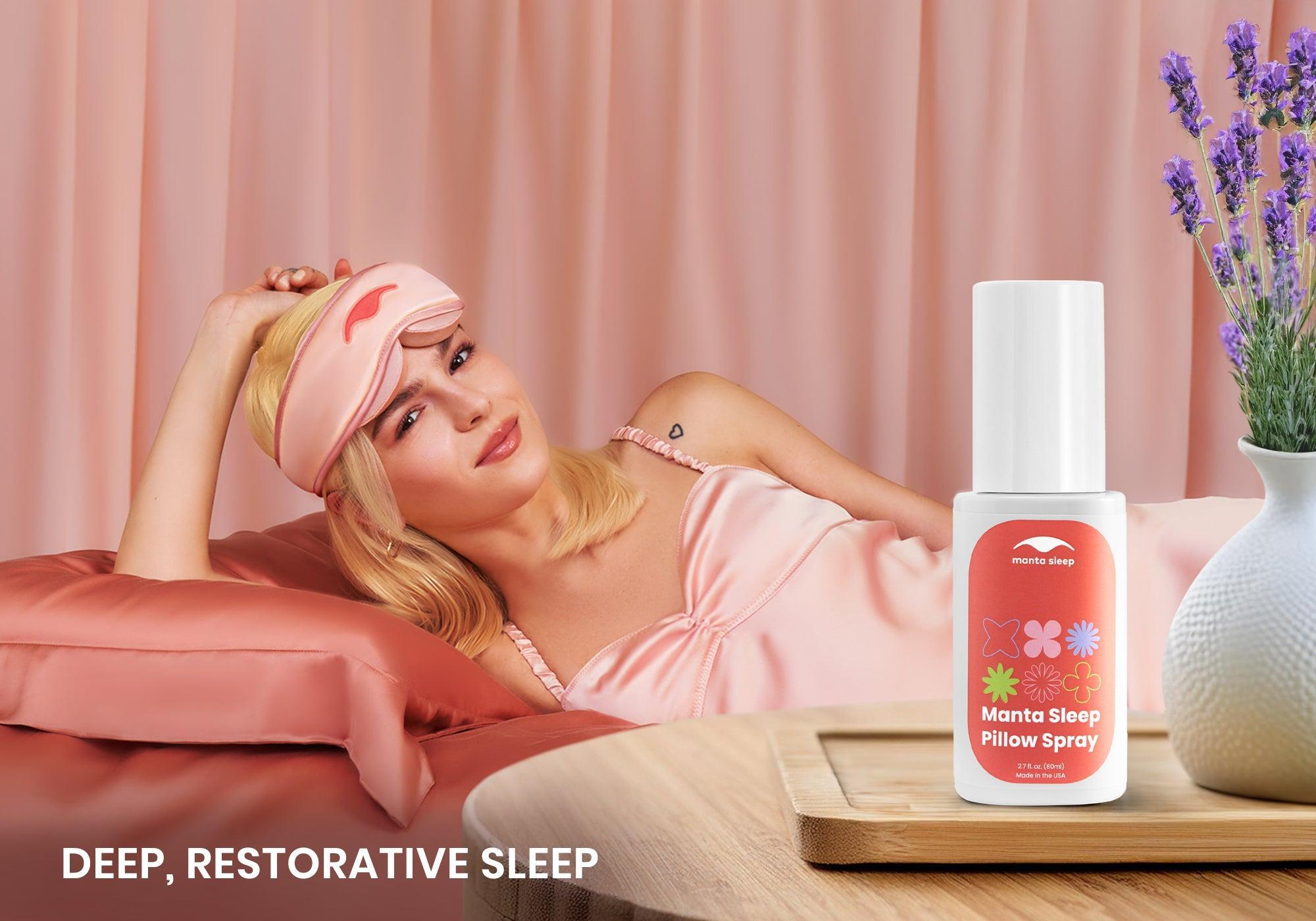A woman resting on a bed with pink Manta SILK Sleep Mask on a forehead, white Manta Pillow Spray on the nightstand in the foreground. Text overlay: Deep, restorative sleep.
