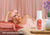 A woman resting on a bed with pink Manta SILK Sleep Mask on a forehead, white Manta Pillow Spray on the nightstand in the foreground. Text overlay: Deep, restorative sleep.