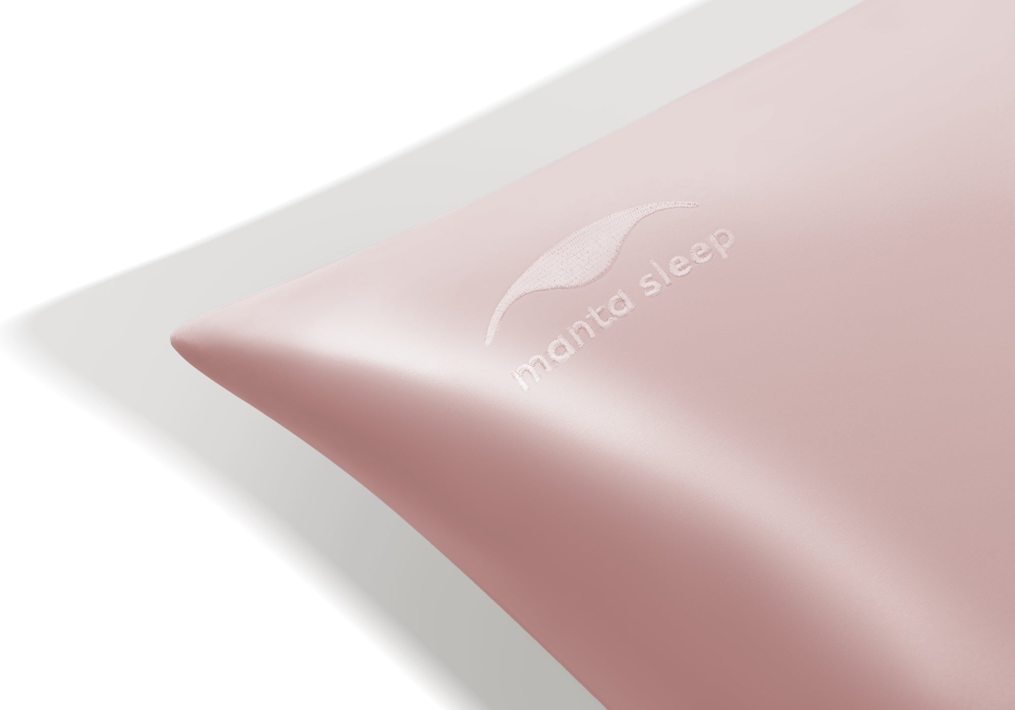 Extreme close-up of the tonal, embroidered Manta Sleep logo on the corner of a rose pink silk pillowcase.