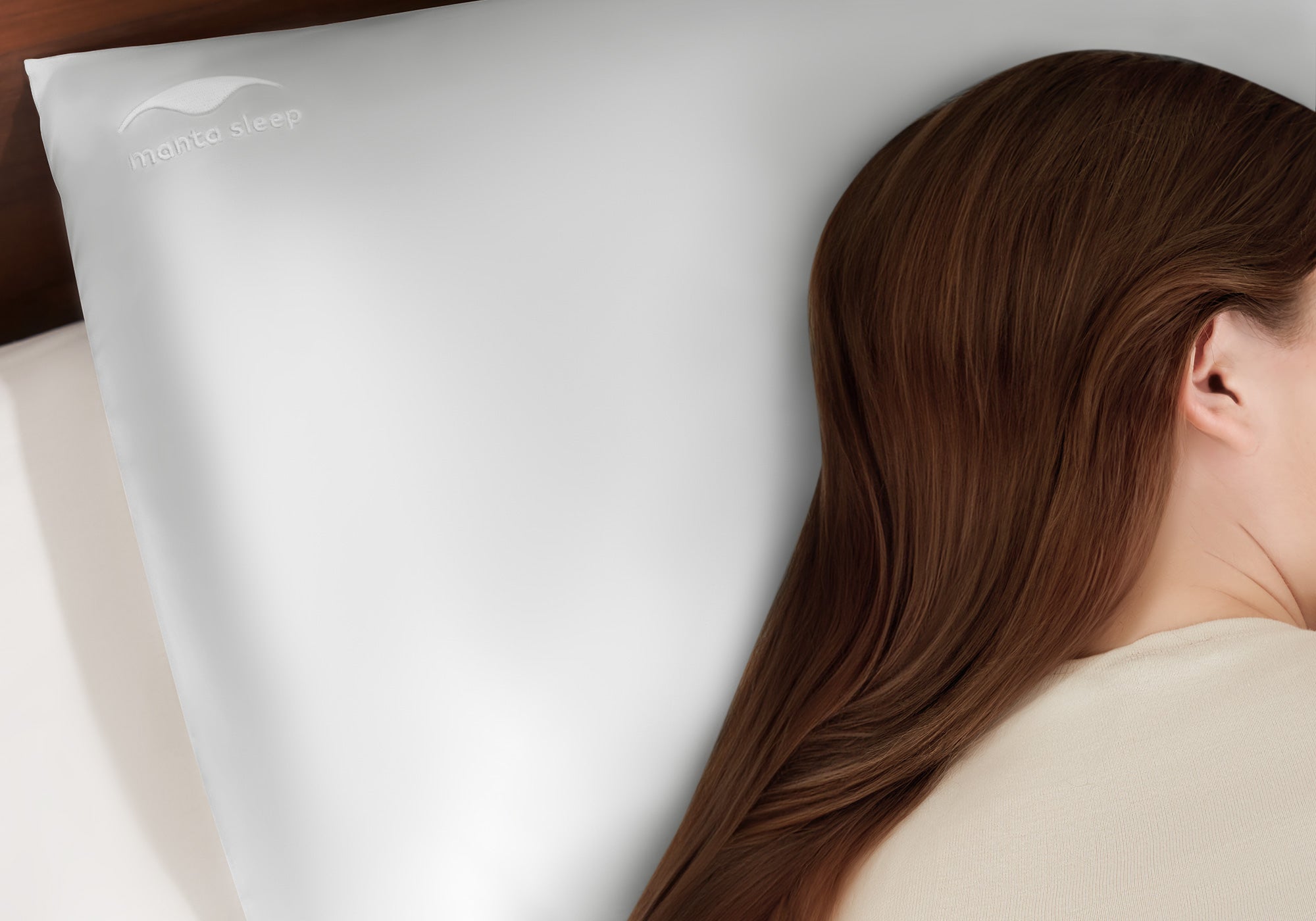 Close-up profile of a woman with long, smooth brown hair resting on a crystal silver Manta Sleep silk pillowcase.