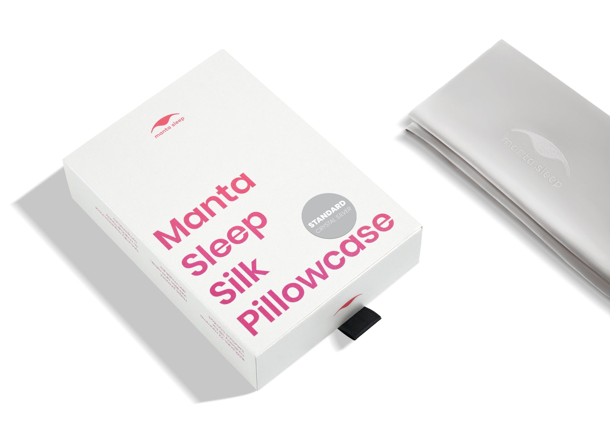 High-angle shot of the white product box with pink text and a folded crystal silver Manta Sleep silk pillowcase.