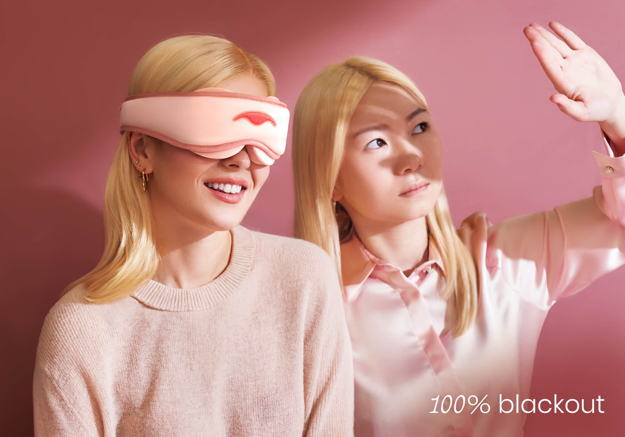 One person smiling in a pink sleep mask next to another shielding their eyes from bright light. Text overlay reads "100% blackout".