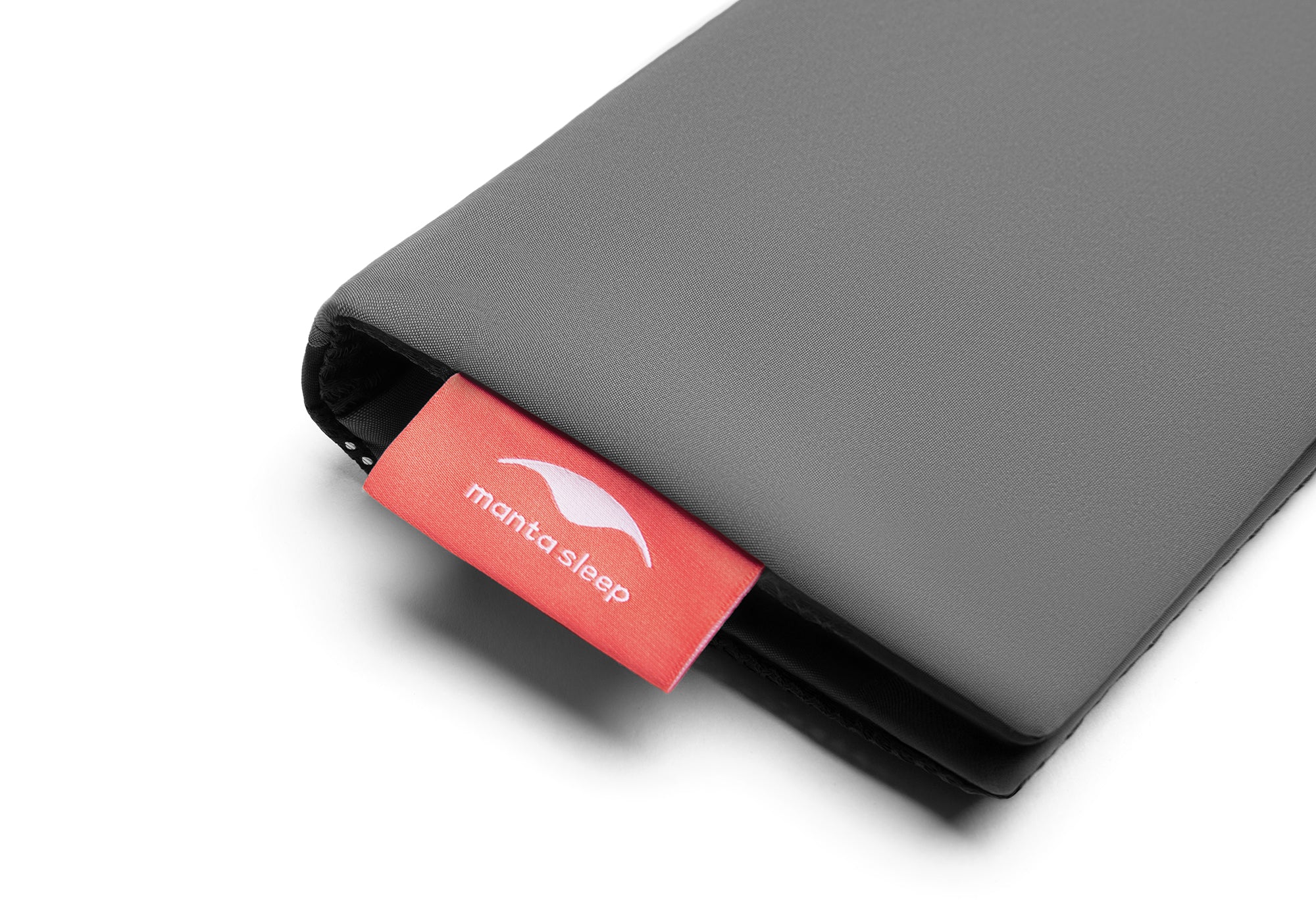Close-up view of the corner of the folded grey pouch focusing on a bright red fabric tag with the white Manta Sleep logo.
