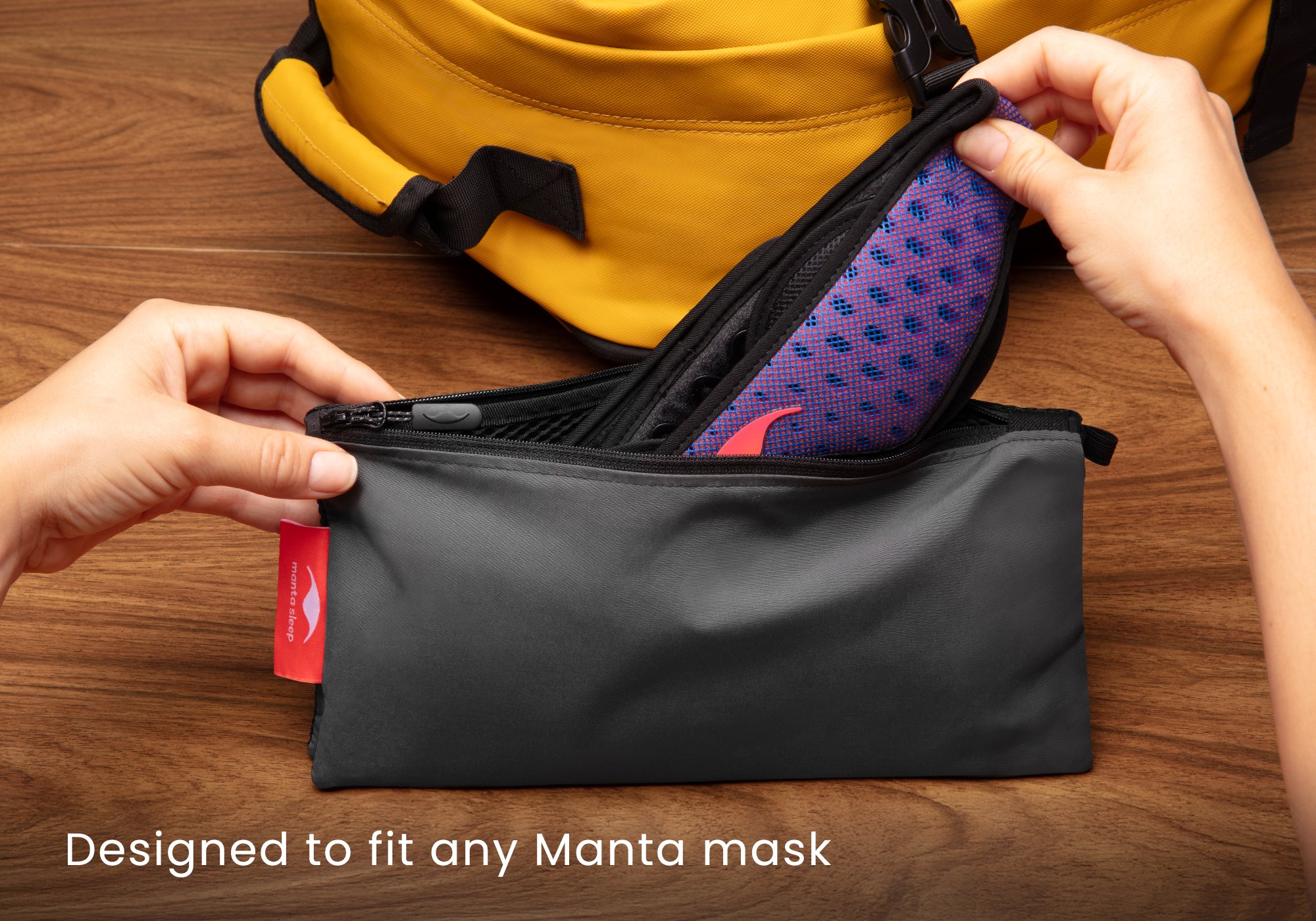 Hands placing a blue and red Manta PRO Sleep Mask into the grey zippered travel pouch, with a yellow backpack in the background. Text overlay: "Designed to fit any Manta mask".