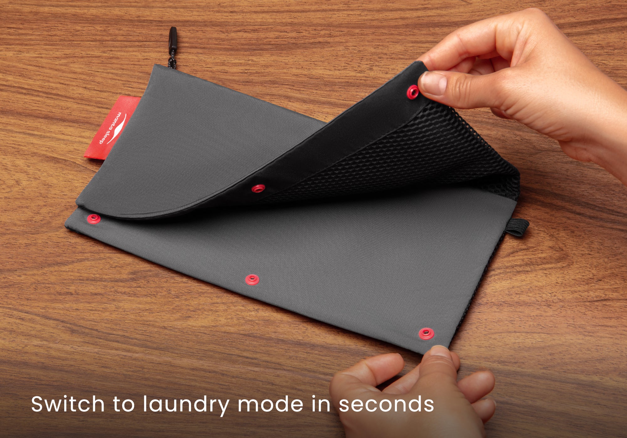 Hands unfastening the red snap buttons to unroll the grey pouch from compact travel mode into a large mesh wash bag. Text overlay: "Switch to laundry mode in seconds".