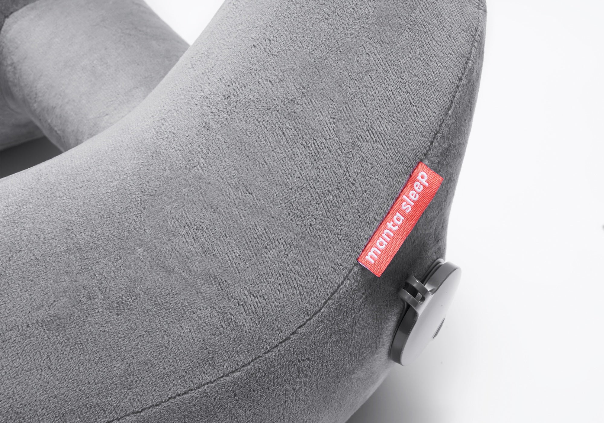 Close-up view of a grey plush travel pillow featuring a red Manta Sleep logo tag and a circular inflation valve.