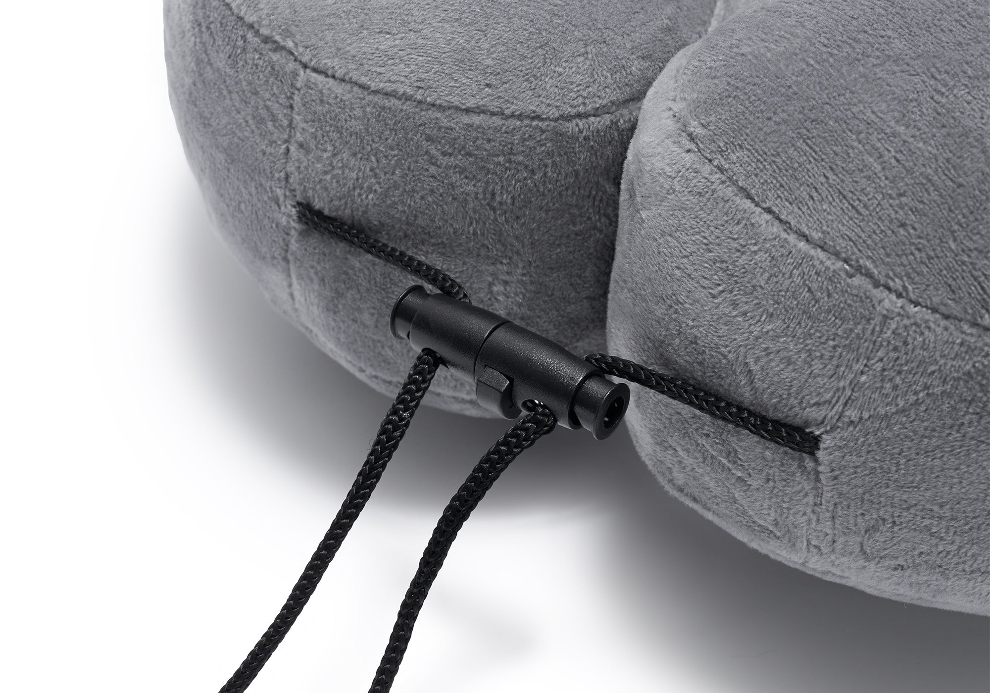 Extreme close-up of the adjustable black plastic drawstring toggle on a grey plush travel pillow.