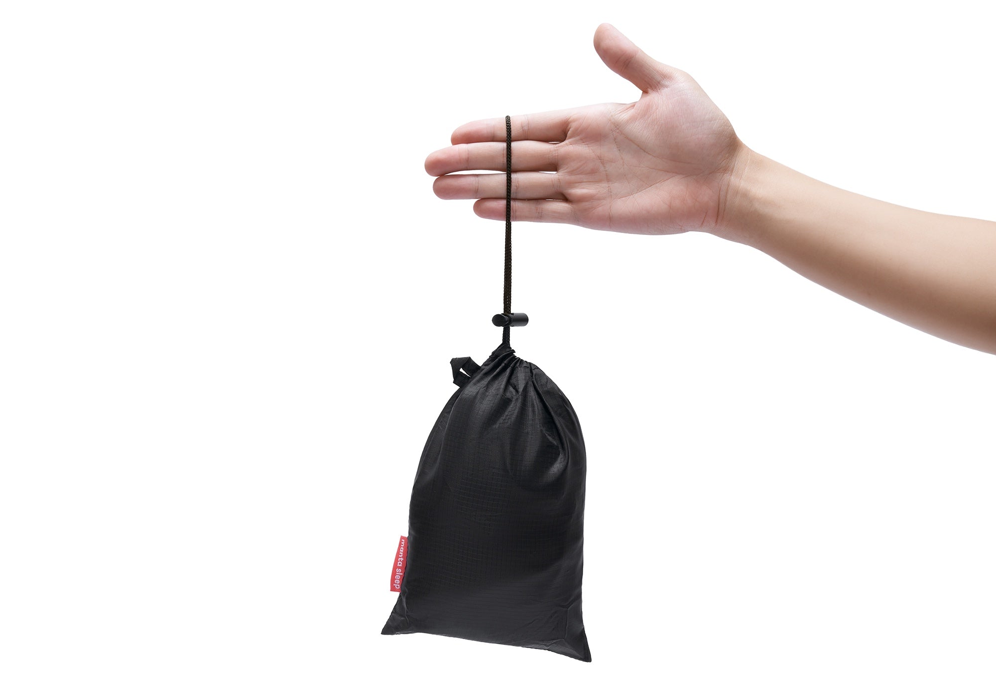 Side view of a hand holding a compact black drawstring pouch containing the deflated pillow against a white background.