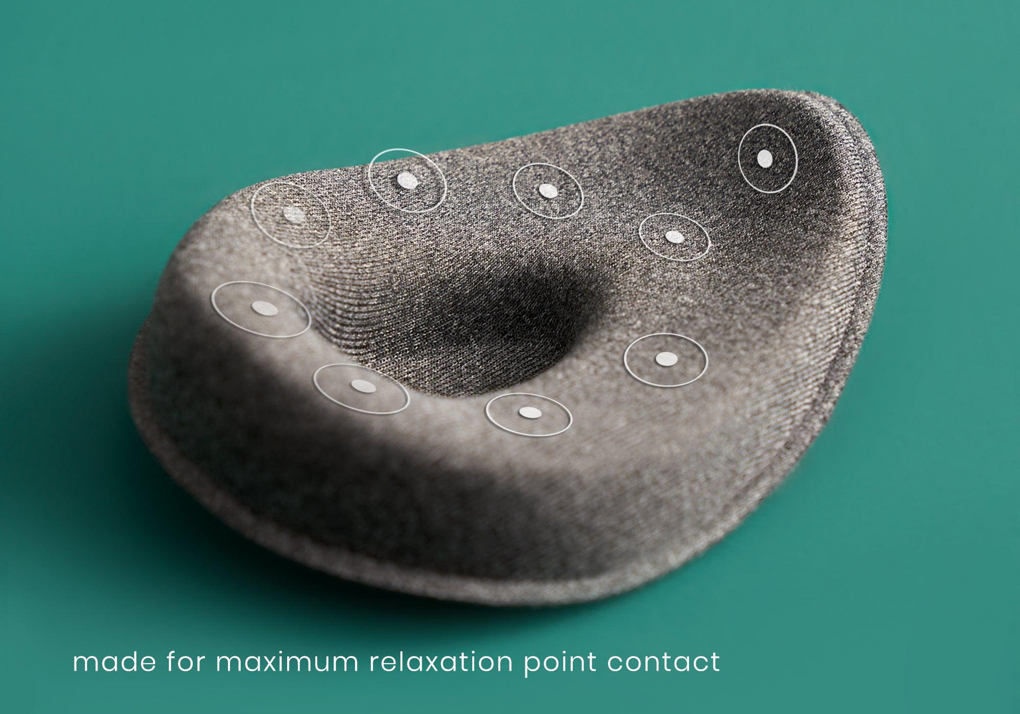 A close-up product feature shot of a single heather-gray modular eye cup resting on a teal surface. Circular graphics with white center dots overlay the cushioned rim of the cup to map out the targeted pressure points. White text at the bottom left reads, "made for maximum relaxation point contact."