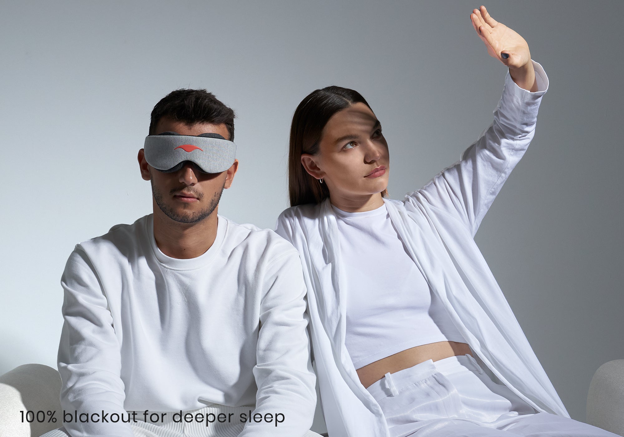 One person in a sleep mask next to another shielding their eyes from direct light. Text reads "100% blackout for deeper sleep".