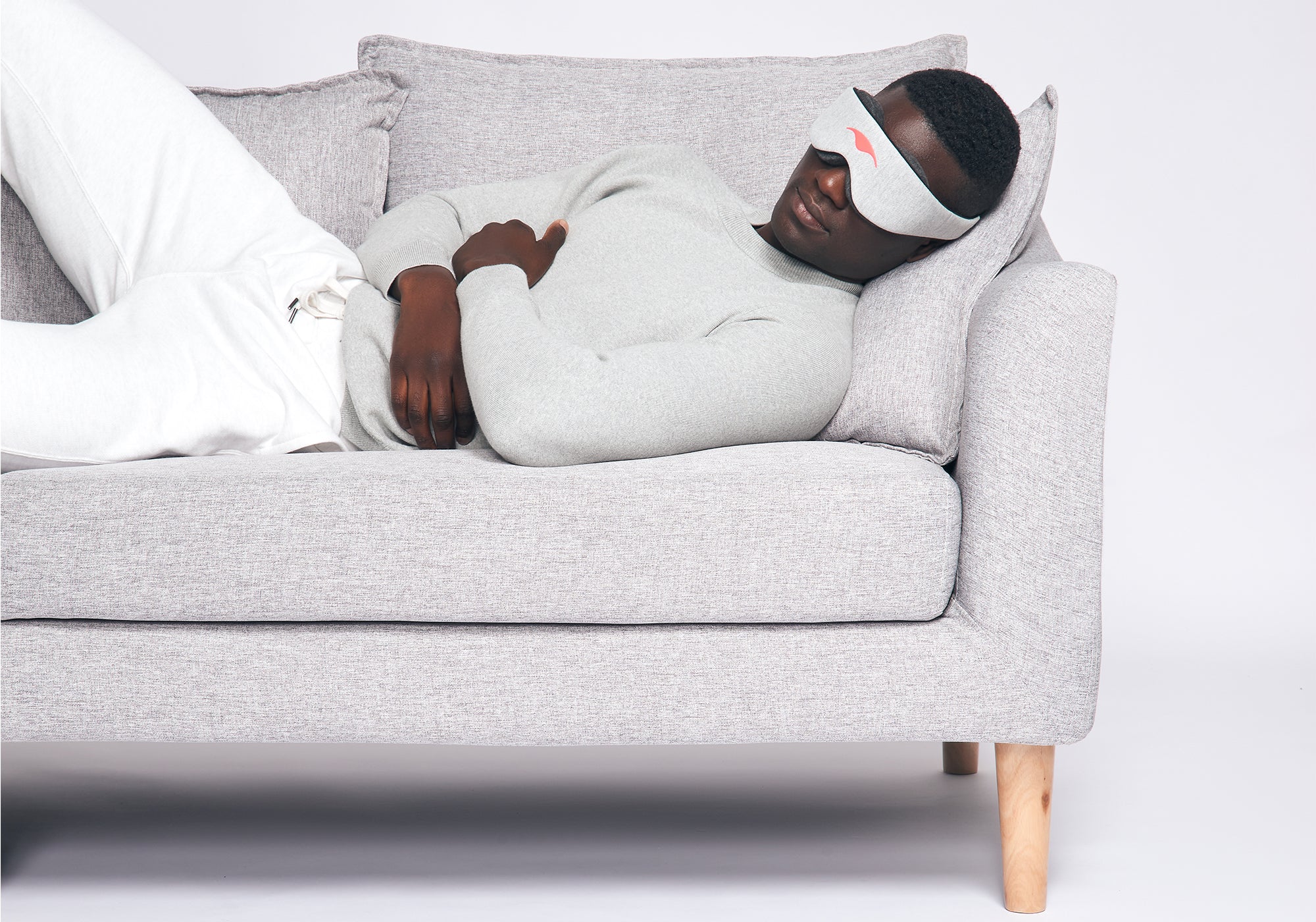 A person relaxing on a light grey fabric sofa while wearing a heather grey Manta Sleep Mask Classic.