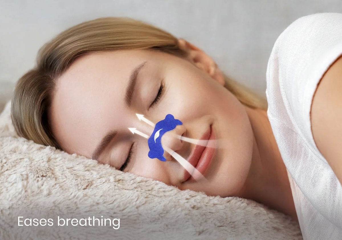 Close-up of a smiling woman sleeping on a plush pillow with a blue nasal strip on her nose and airflow graphics. Text overlay: "Eases breathing".