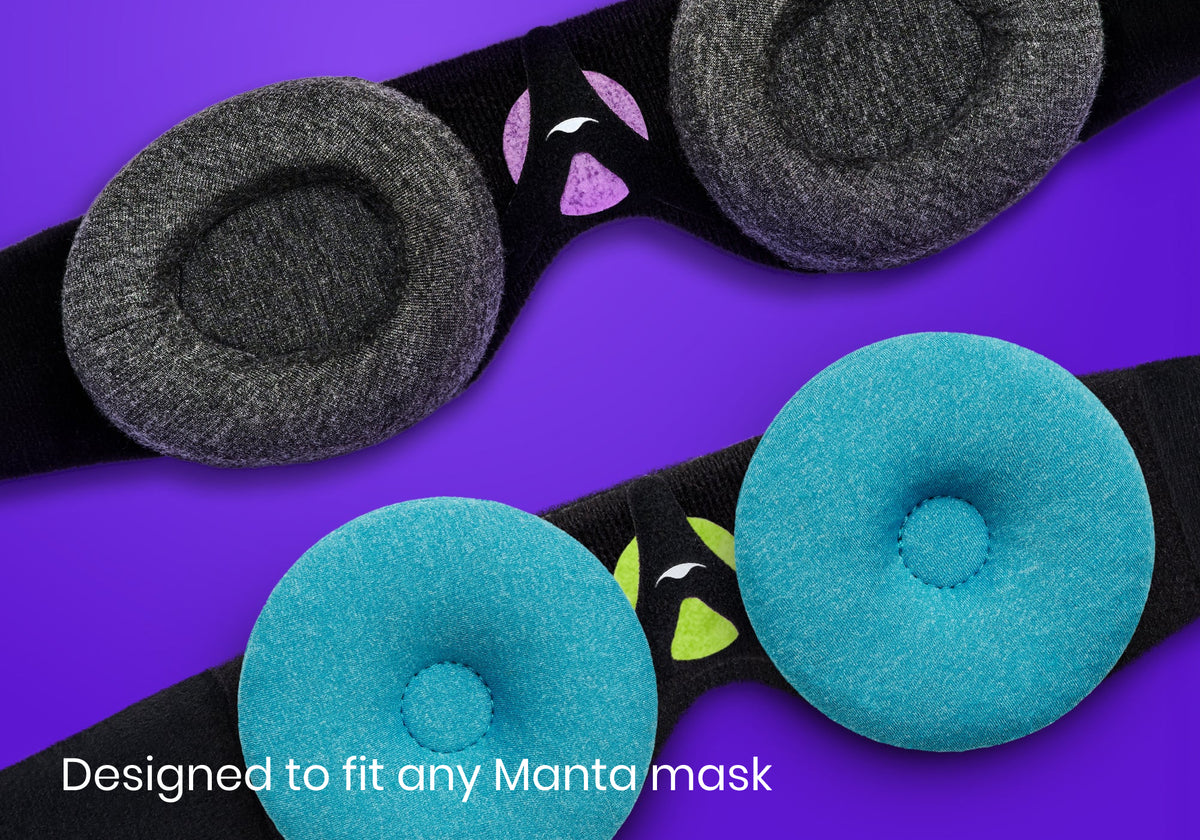 Two black Manta sleep mask head straps, one fitted with gray eye cups and purple patch holder, and one with blue eye cups and green patch holder.