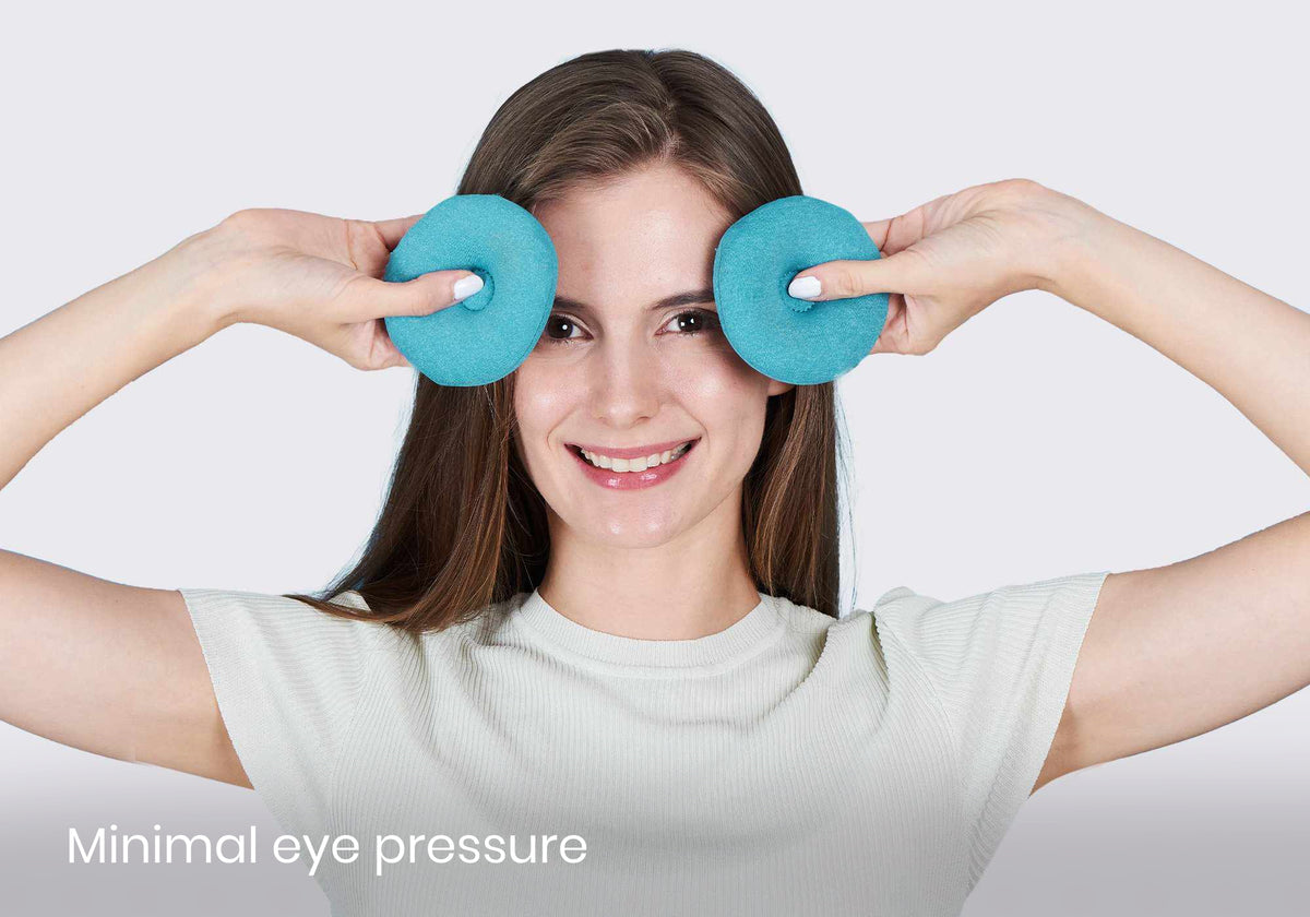 Smiling woman holding two circular blue Manta COOL eye cups in front of her temples, with lower-left text reading "Minimal eye pressure".