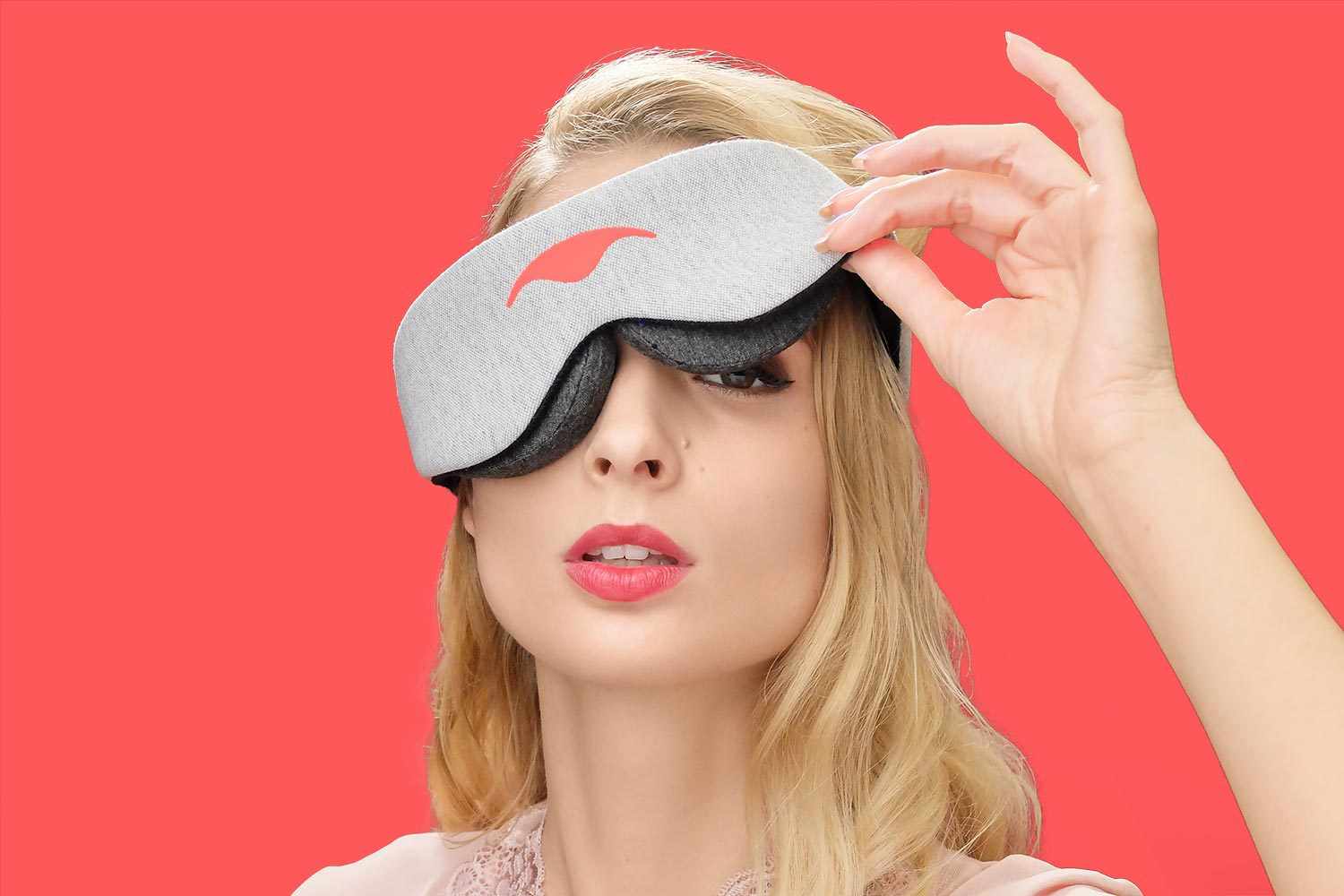Close-up of a person lifting one side of a heather grey Manta Sleep Mask Classic against a solid vibrant red background.
