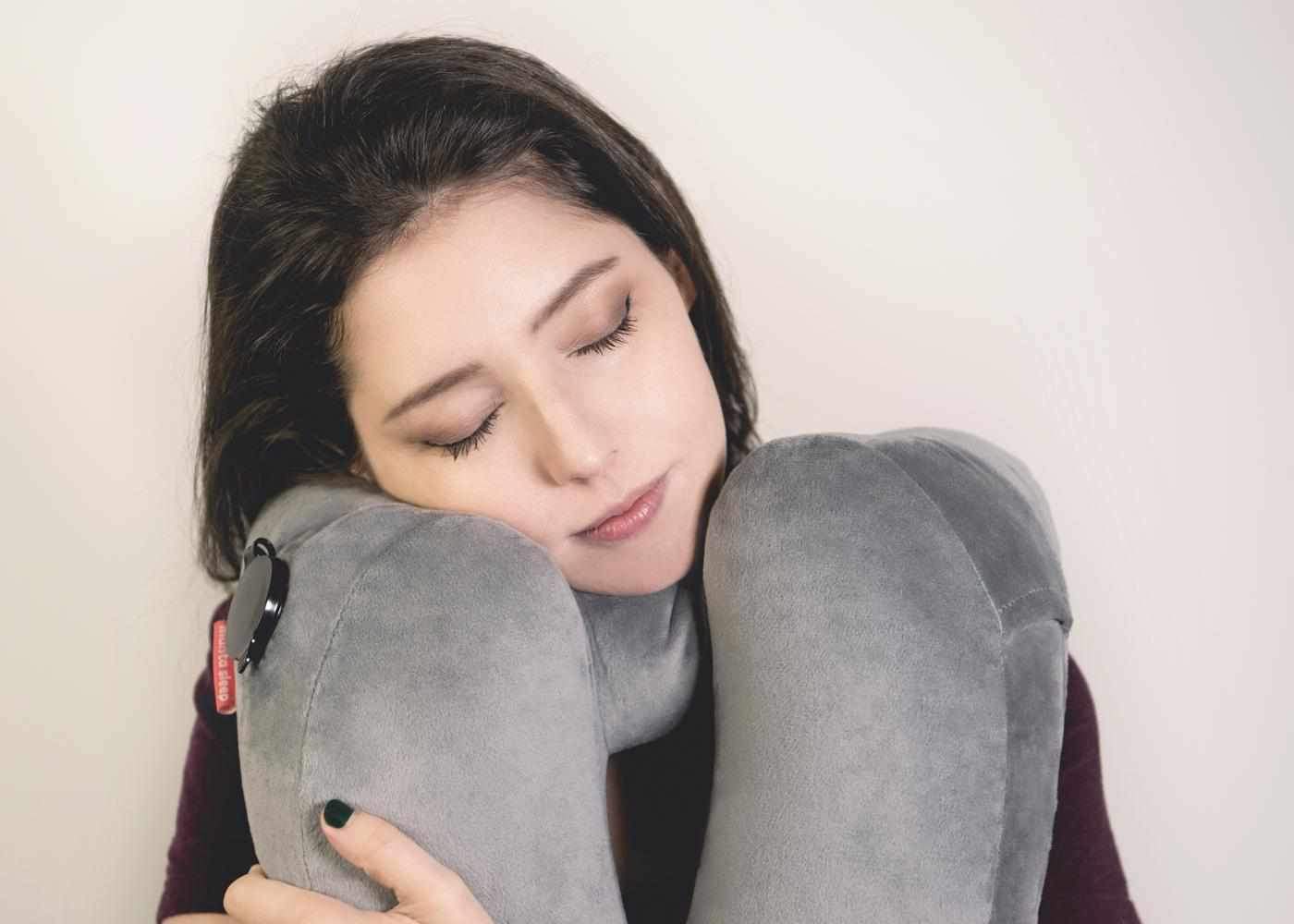 Close-up of a woman hugging a grey plush Manta Travel Pillow while leaning her head against it with eyes closed.