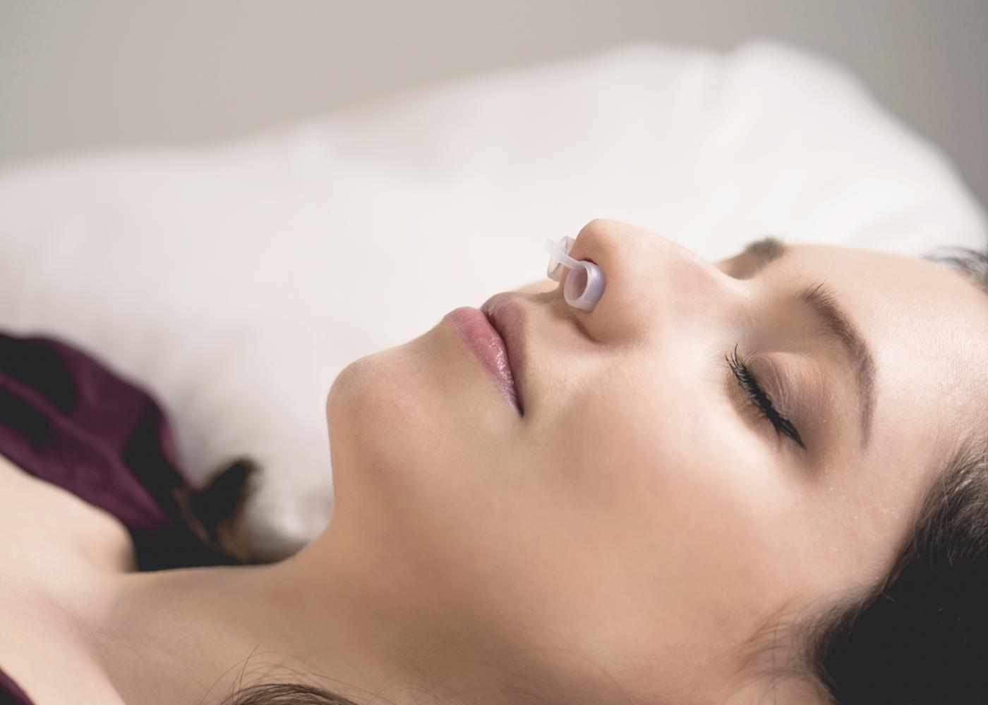 Side profile of a woman sleeping with eyes closed, wearing a clear Manta Sleep Anti-Snore Nose Vent in her nostril.