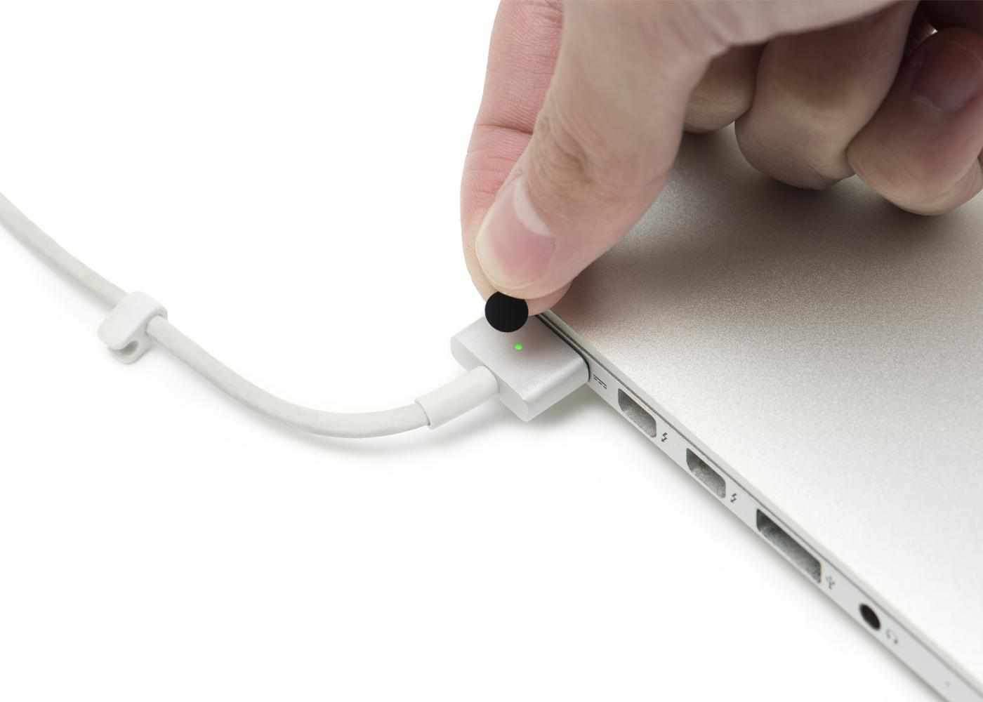 Close-up shot of a hand placing a small circular black sticker onto the glowing green LED light of a laptop charging cable.