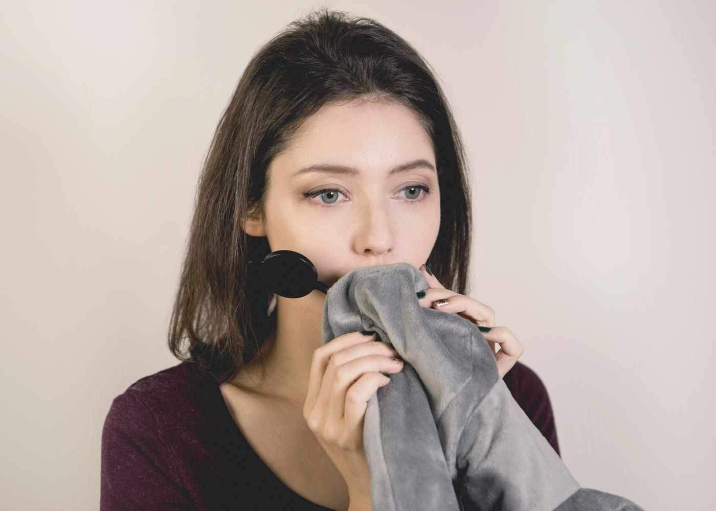 Close-up of a woman blowing into the black inflation valve of a grey plush Manta Travel Pillow.