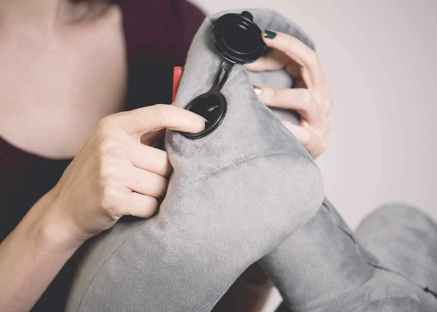 Close-up of hands opening the black fast-inflate valve on a grey plush Manta Travel Pillow.