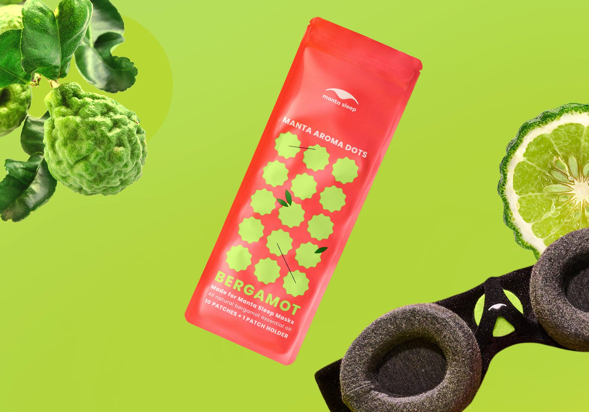 Bergamot-scented Manta Aroma Dots packaging floating with whole and sliced bergamot fruit next to a sleep mask, on a lime green background.