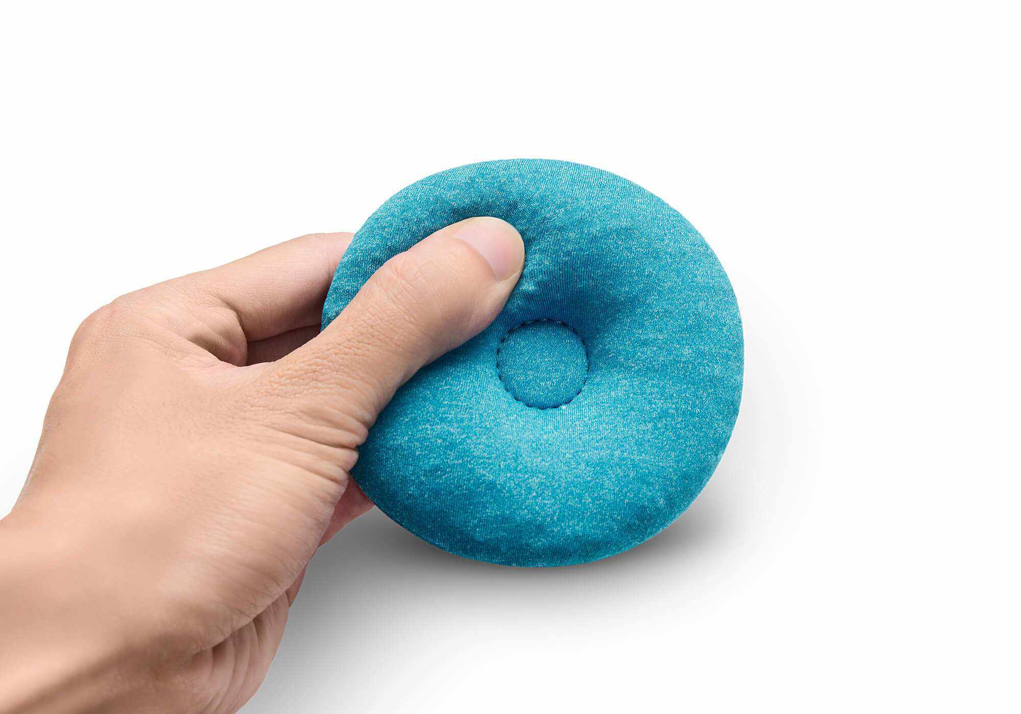 A hand squeezing a soft, round blue-teal fabric eye cup to demonstrate its moldable material, isolated on white.