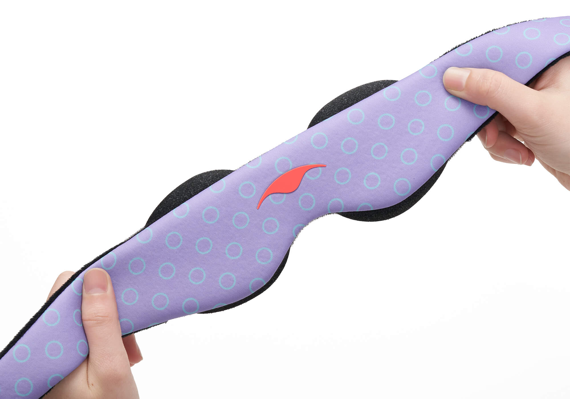 A close-up view of two hands stretching the flexible, elastic head strap of a purple Manta KIDS Sleep Mask against a clean white background. The mask features a pattern of light blue open circles and a small orange Manta Sleep logo in the center, showing the flexibility and elasticity of the material.