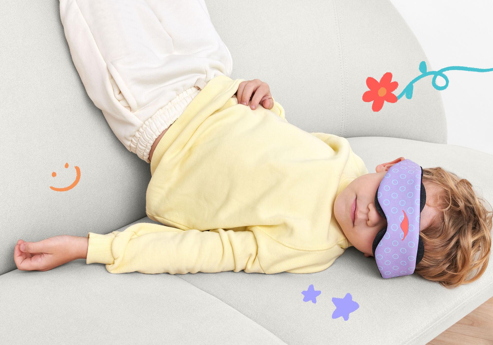 A child with wavy hair wearing a yellow sweatshirt and white sweatpants, resting on a gray sofa while wearing the purple patterned Manta KIDS Sleep Mask over their eyes. The scene is decorated with playful, hand-drawn digital doodles including a smiley face, a flower, and small stars on the background and sofa.