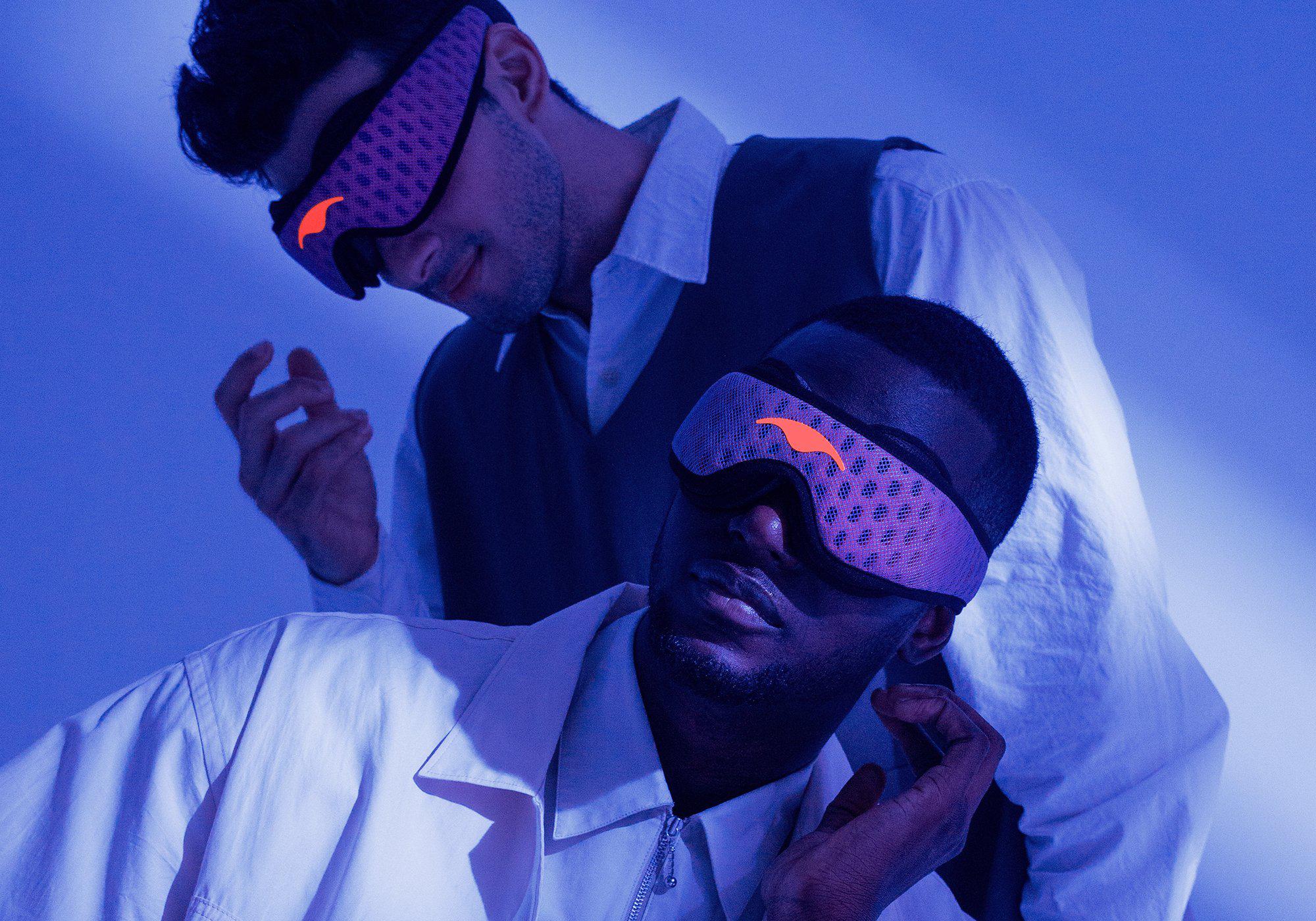 Two men under a cool blue light wearing purple Manta Sleep Mask PROs over their eyes, showcasing the comfortable blackout fit.