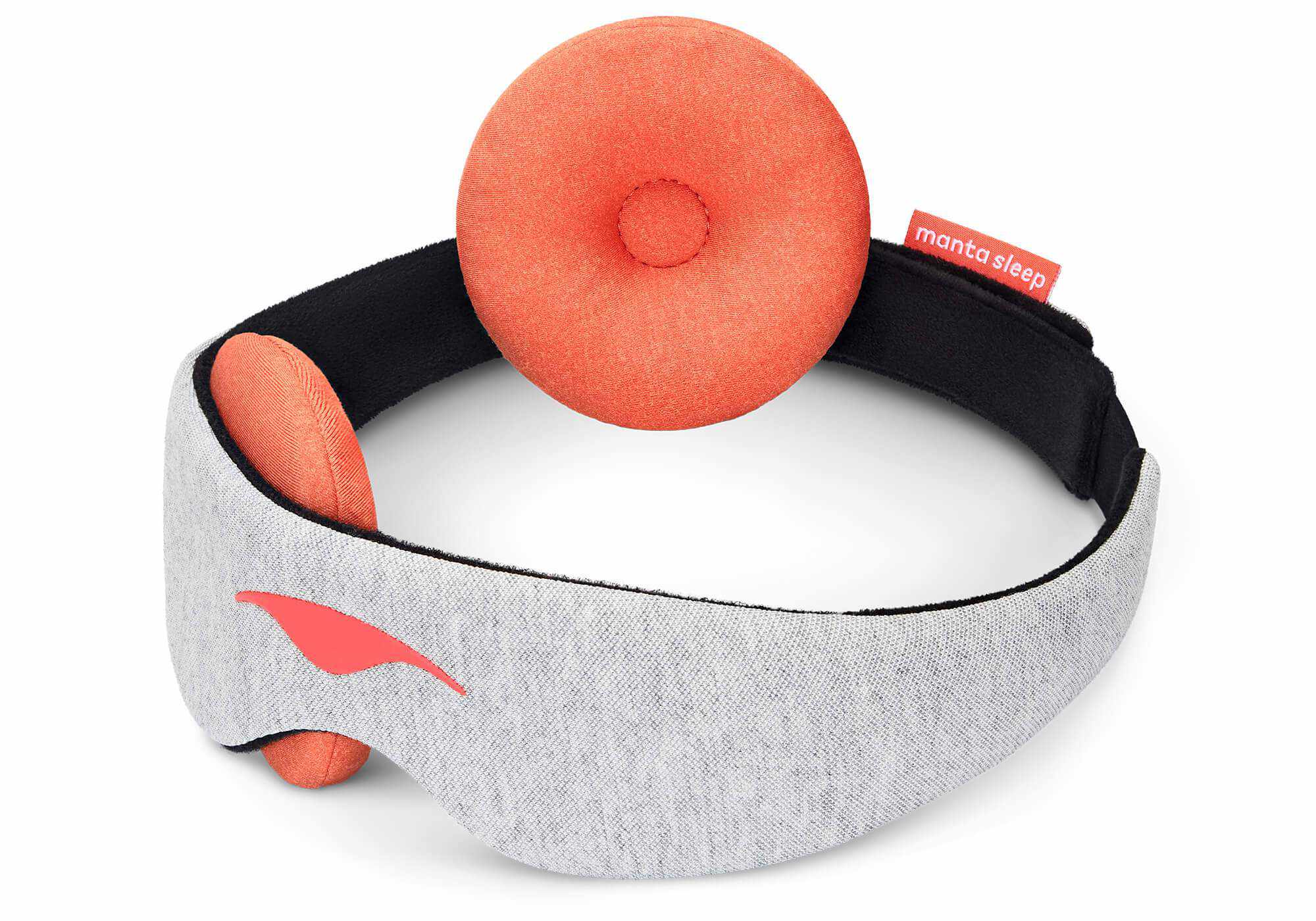 A perspective product shot of the Manta STEAM Sleep Mask looped over a white background. One of the plush, circular terracotta-orange eye cups is detached and turned outward to showcase its soft rim and indented center, while the main front band remains visible to highlight the gray heathered fabric and coral Manta Sleep logo.