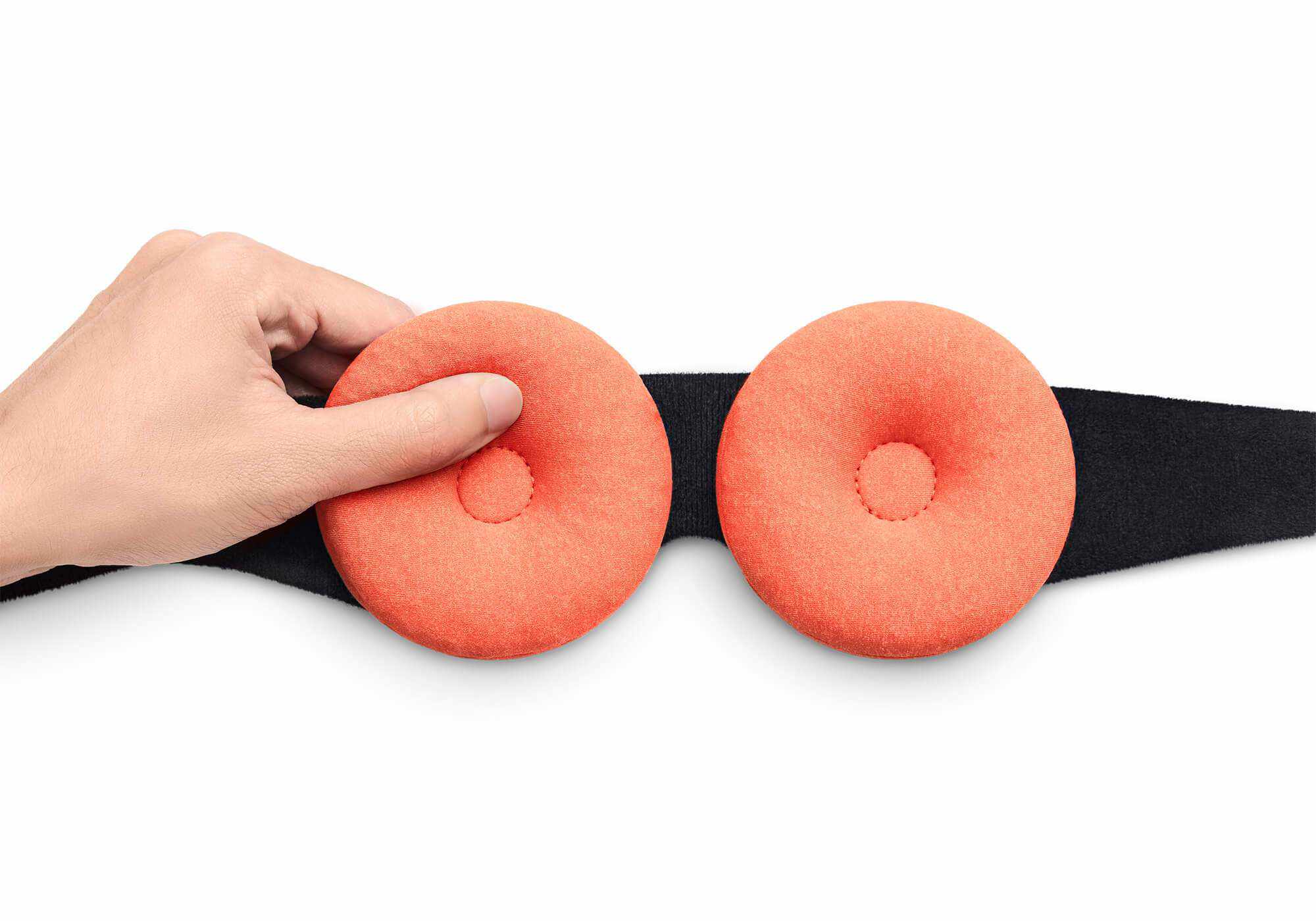 A top-down view focusing on the interior side of the Manta STEAM Sleep Mask against a plain white background. The image displays two thick, circular terracotta-orange eye cups with a dimpled center indentation attached to a black plush fabric backing. A hand adjusts the placement of the left eye cup along the hook-and-loop track.
